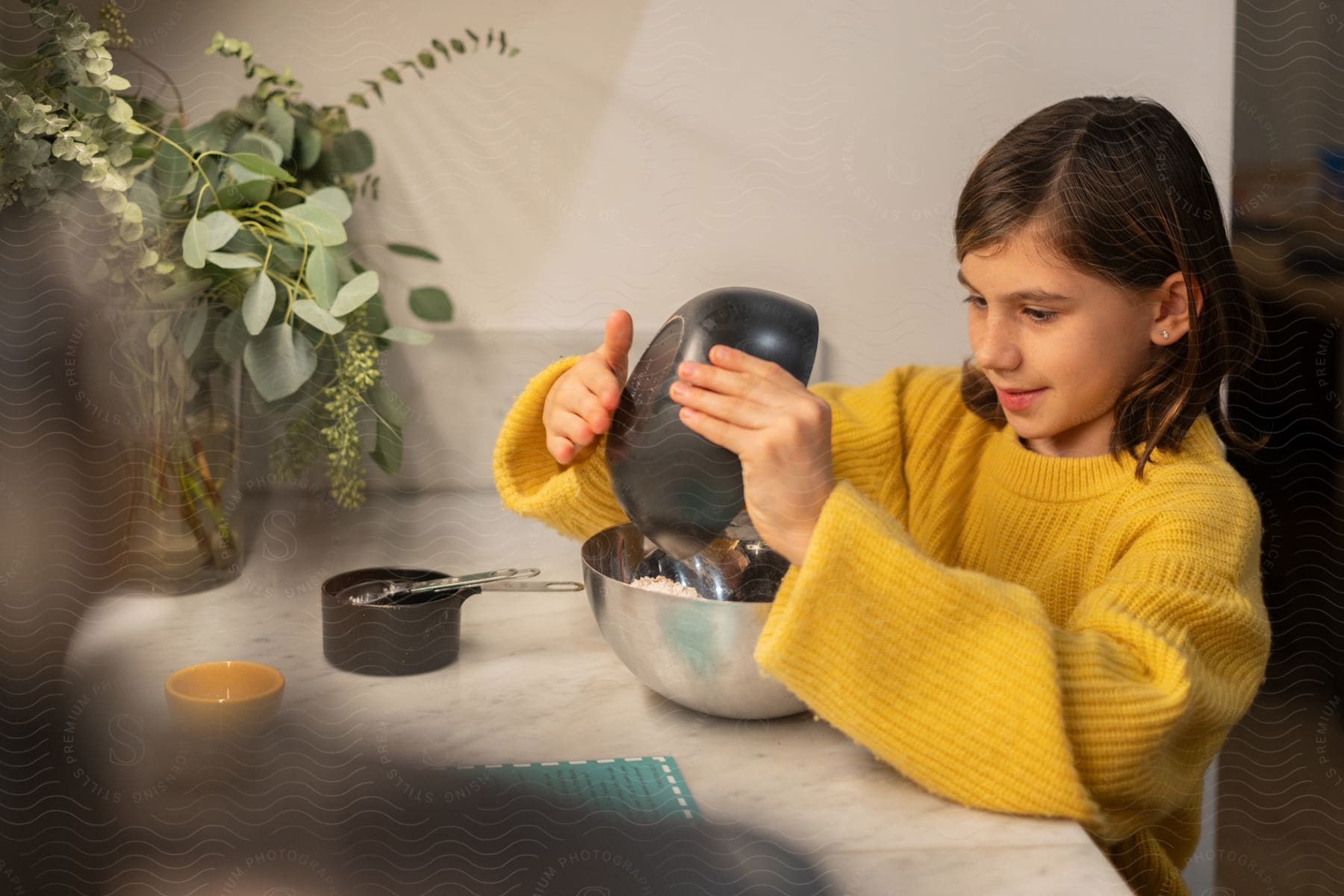 A girl baking food in a kitchen pouring food from a bowl to another.