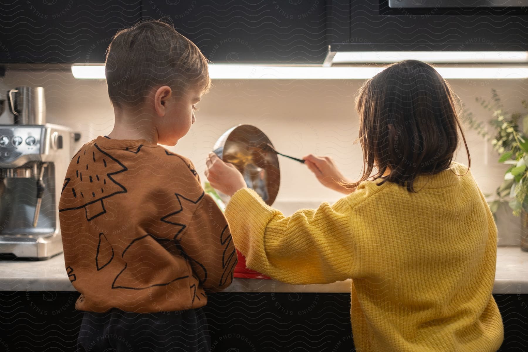 A boy and a girl skillfully skim off a bowl with a knife in the kitchen.