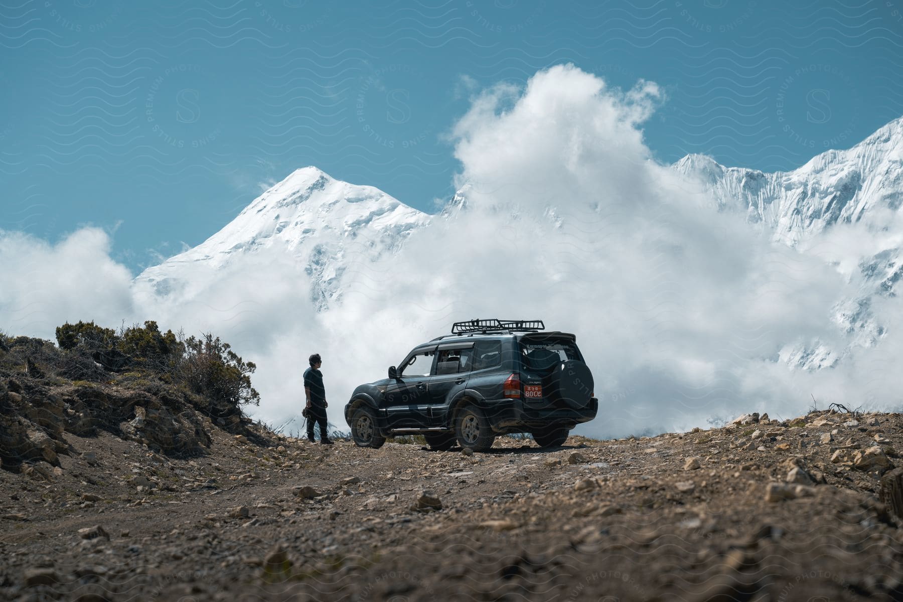 Man stands by Mitsubishi Montero SUV watching snowy mountain range