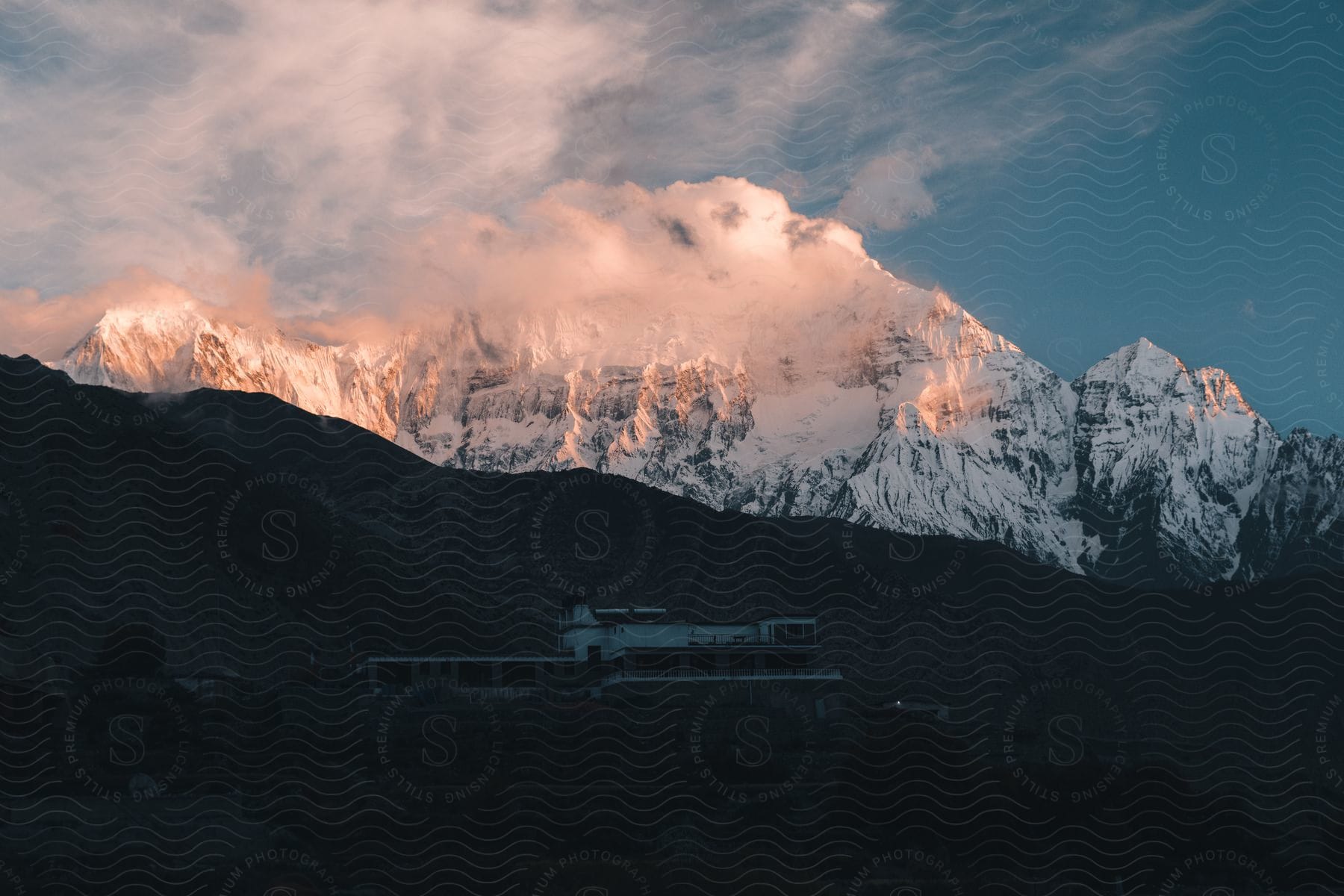 A long building sits at the foot of a mountain with a snow covered mountain in the distance