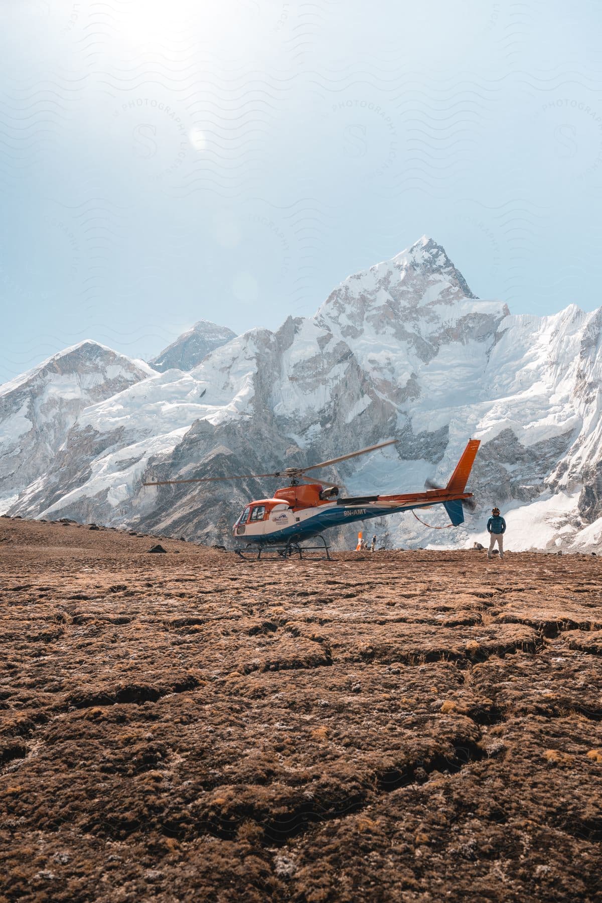 Helicopter on the ground with a person beside it amid snow-covered mountains.