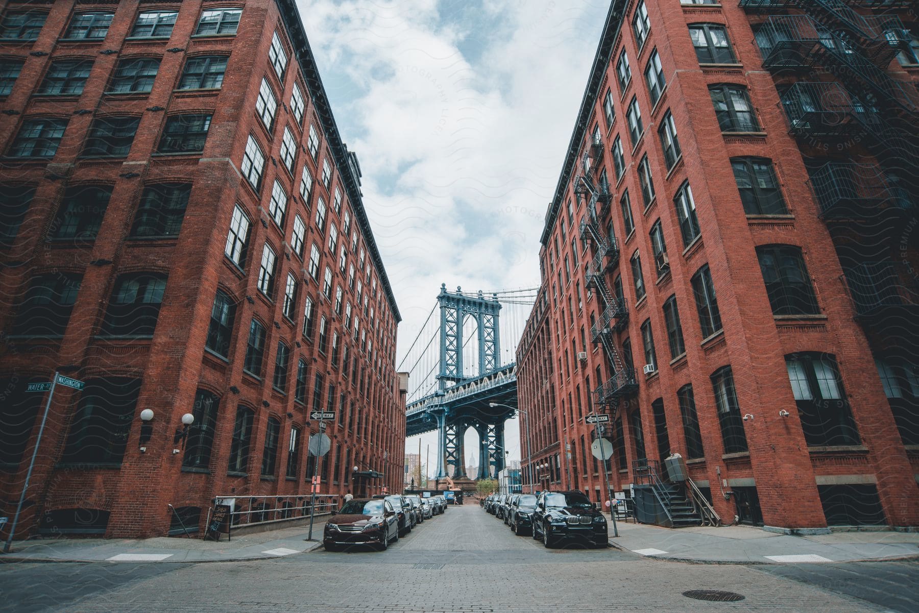 Cars line a red-brick Brooklyn street, with the iconic bridge in the distance.