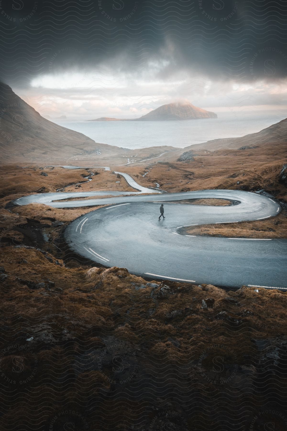 Distant man walking down winding highway to the coast with a small island in the background