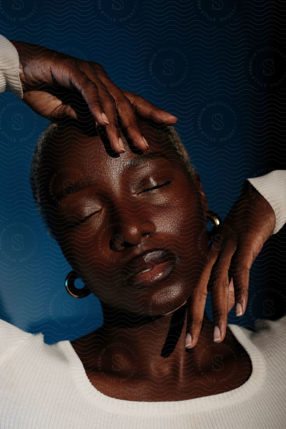 A woman poses with one hand near her chin and the other on top of her head with her eyes closed