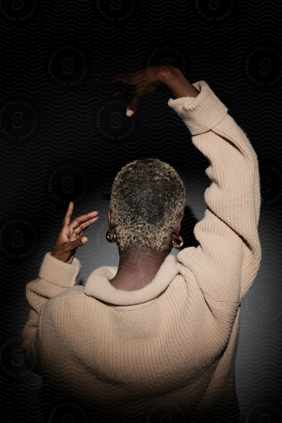 Back view of a model woman wearing a wool sweater in a dark environment.