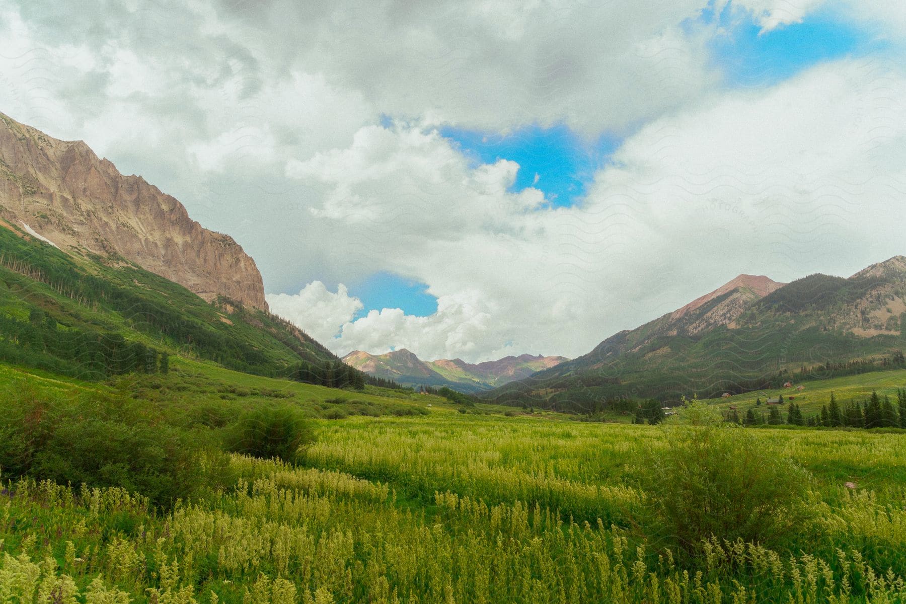 Mountains surround a grassy valley under a cloudy blue sky.
