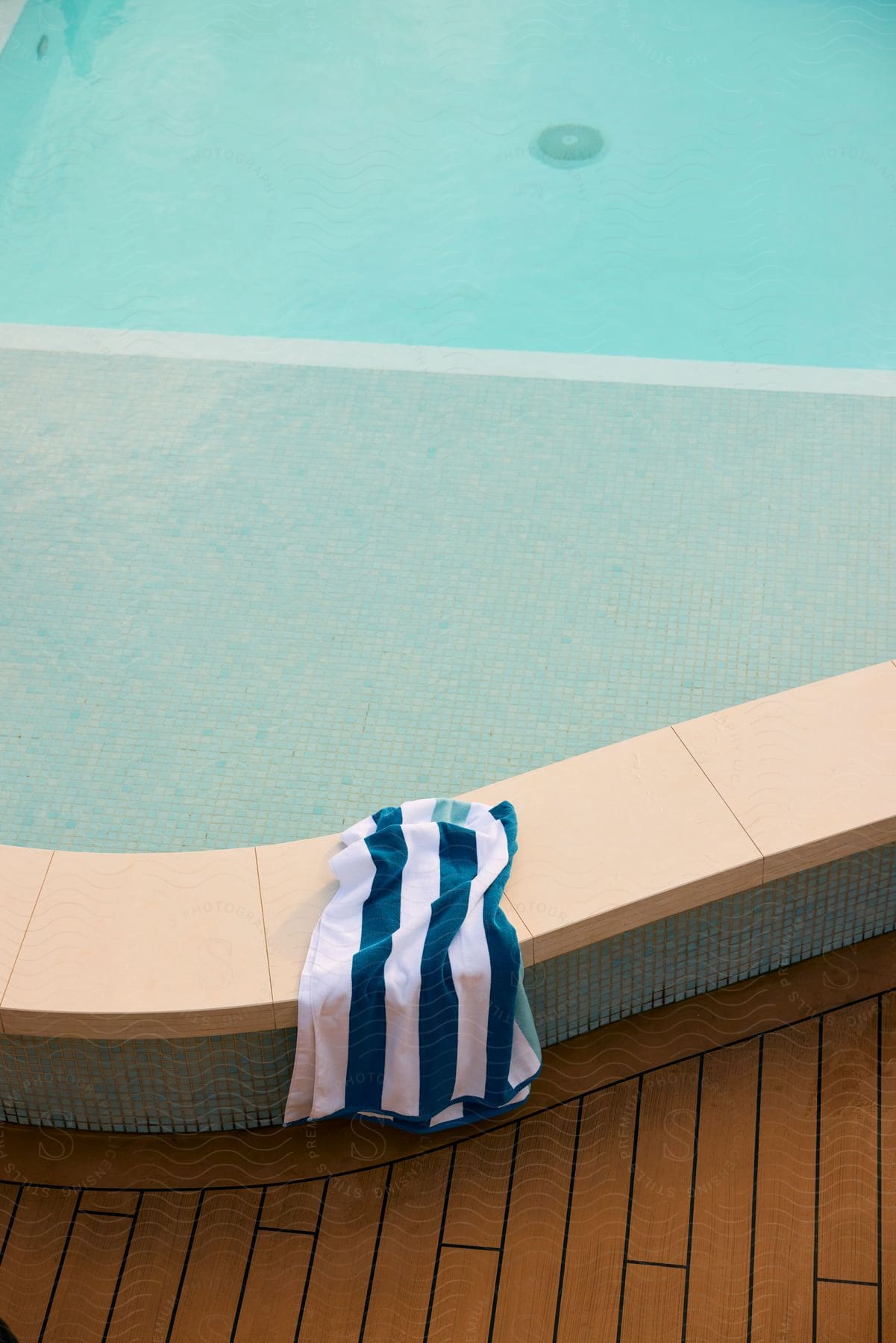 A striped towel drapes over a pool edge against a wooden deck.