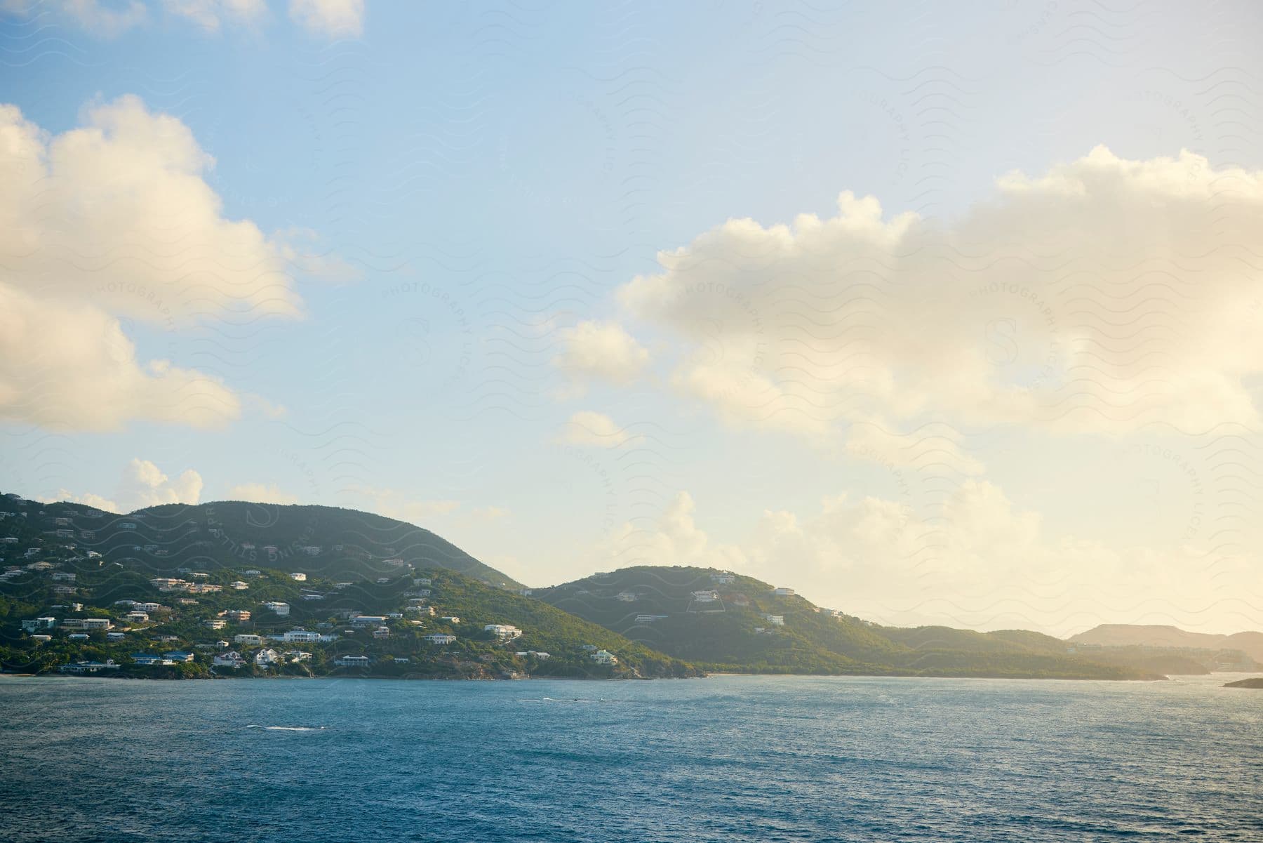 A coastal seascape with houses dotting the hillside under a sky with scattered clouds.