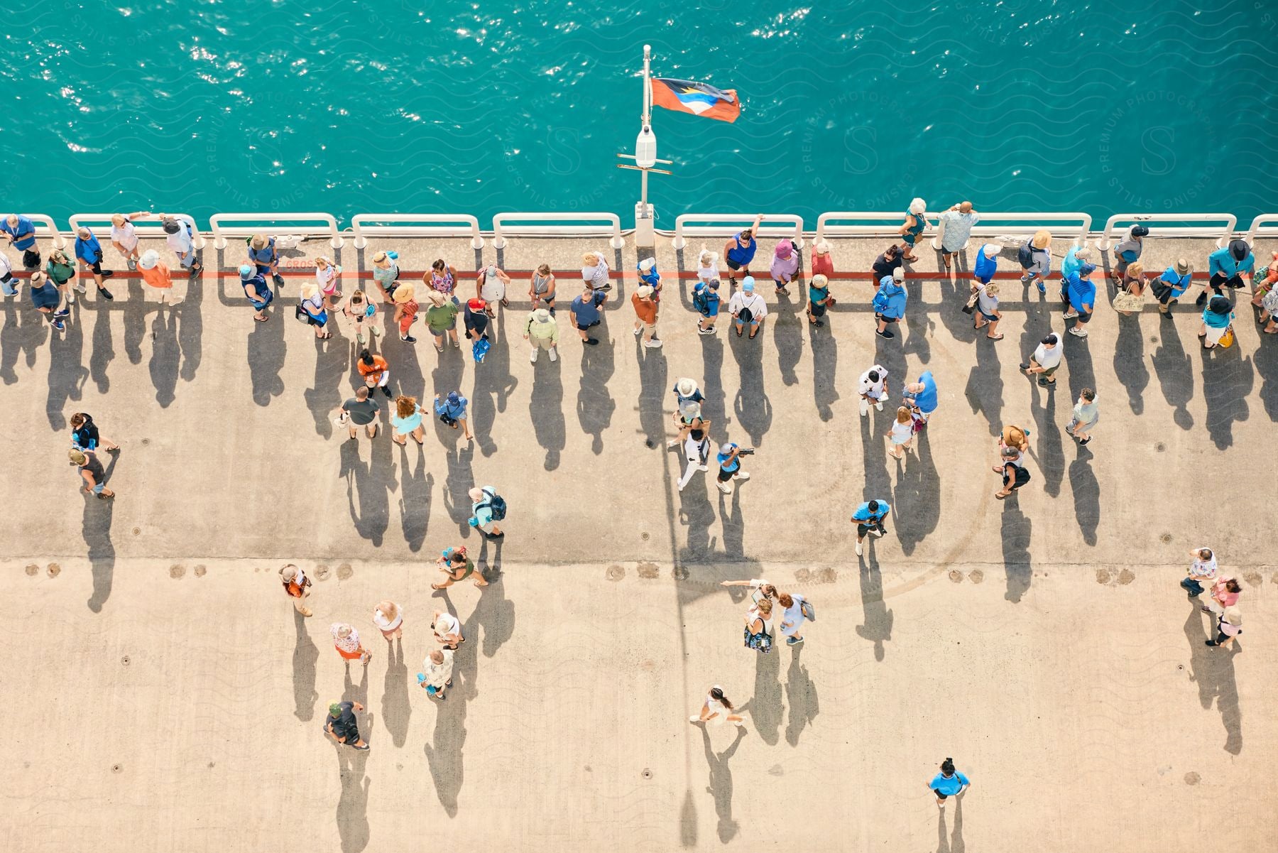 People gather on a pier, enjoying the ocean breeze under a waving flag.