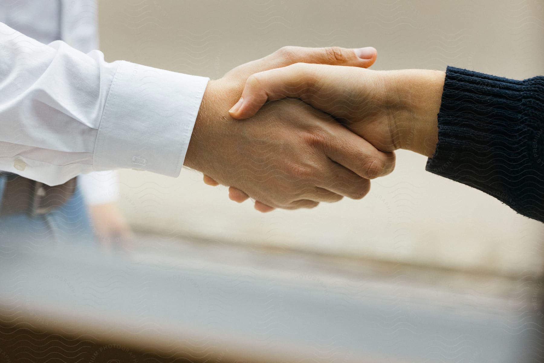 A professional in a white button-up shirt and jeans shakes hands with a casually dressed individual in a black long-sleeve sweater.