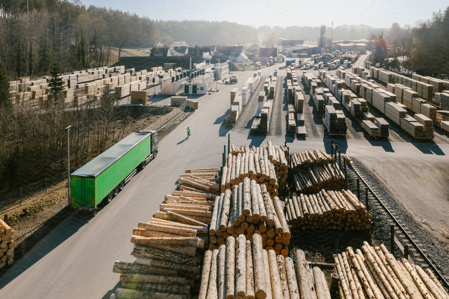 Truck on the road at a lumber yard with stacked wood as a person walks on the street