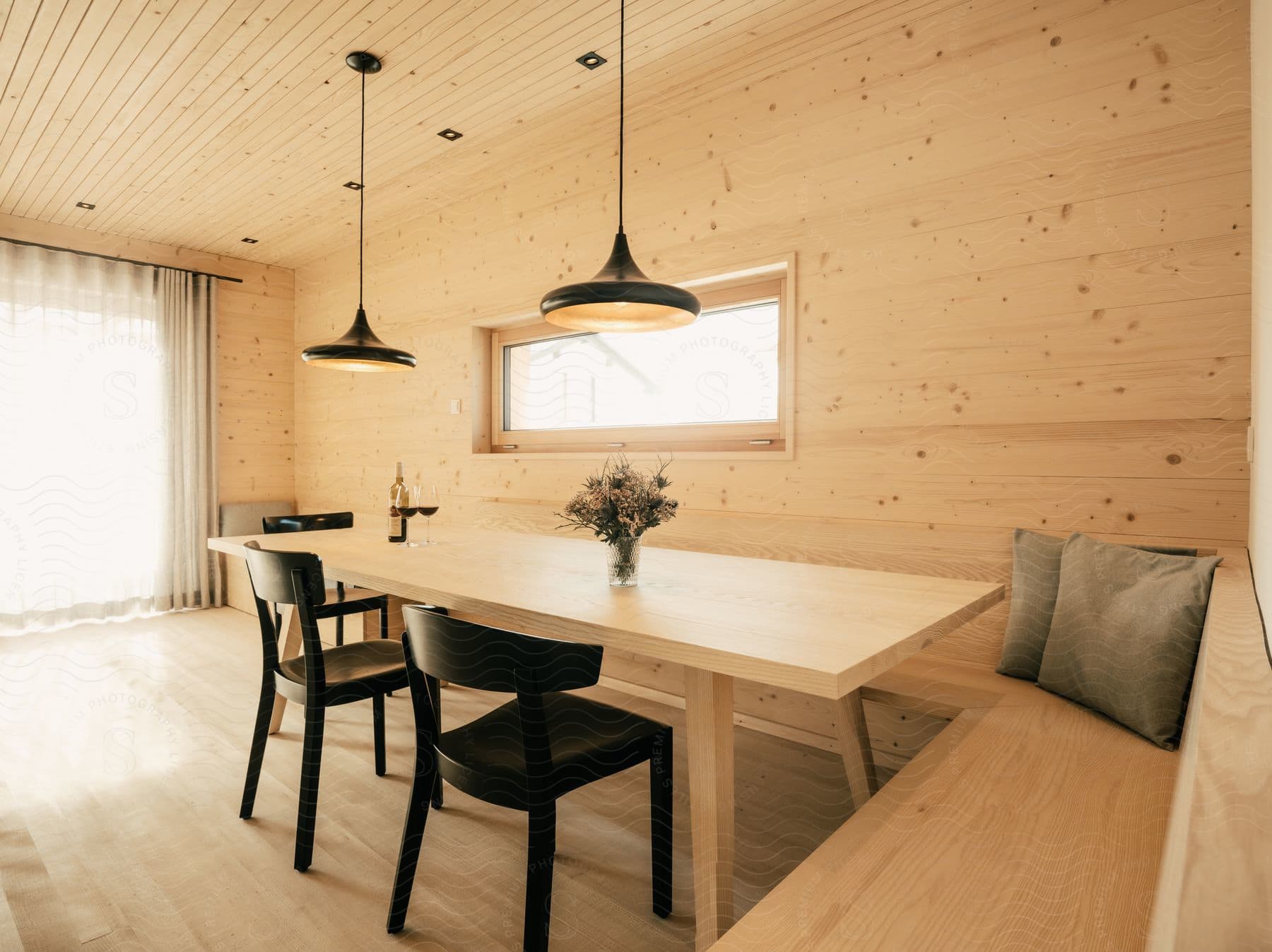 Light wood interior with a table, chairs, bench, cushion, and two pendant lights.