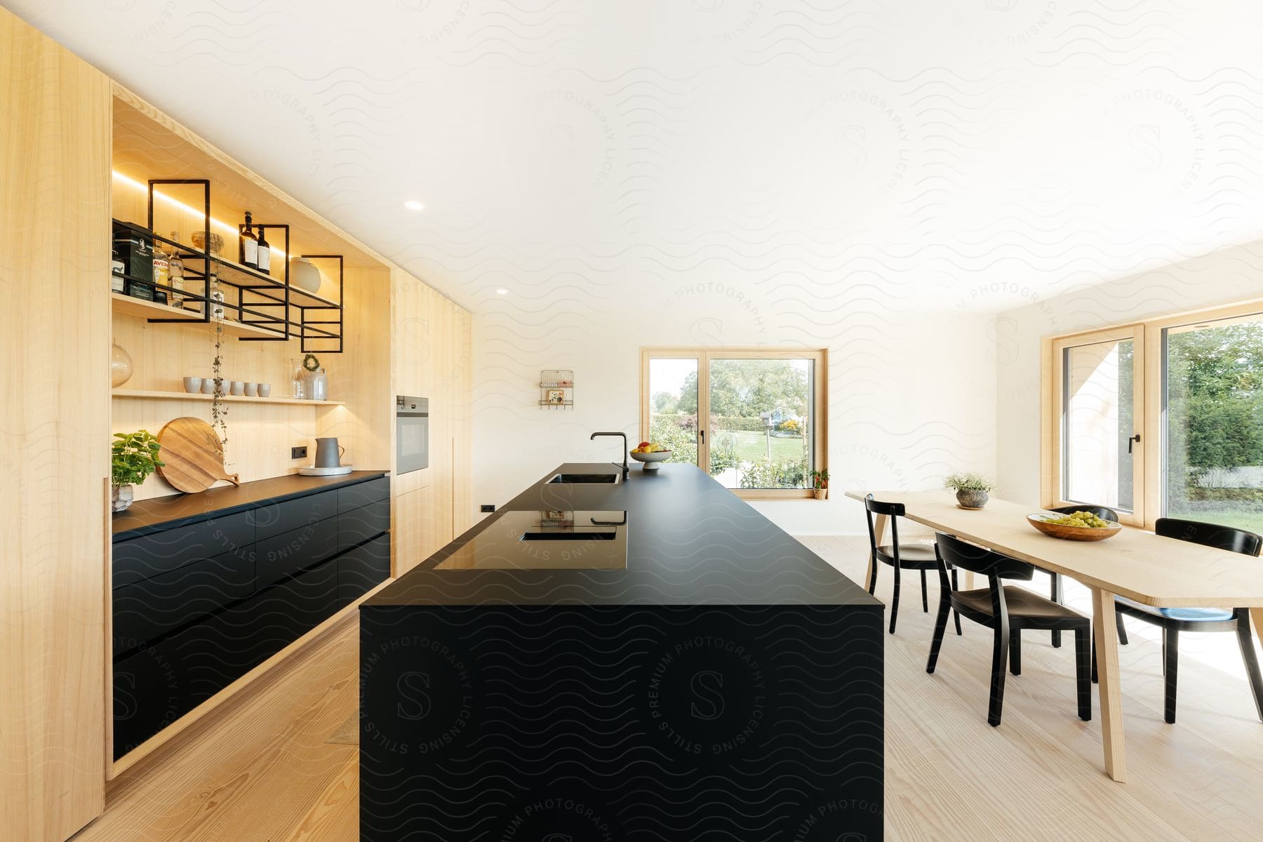 A bright modern kitchen with a black island and a long kitchen table.