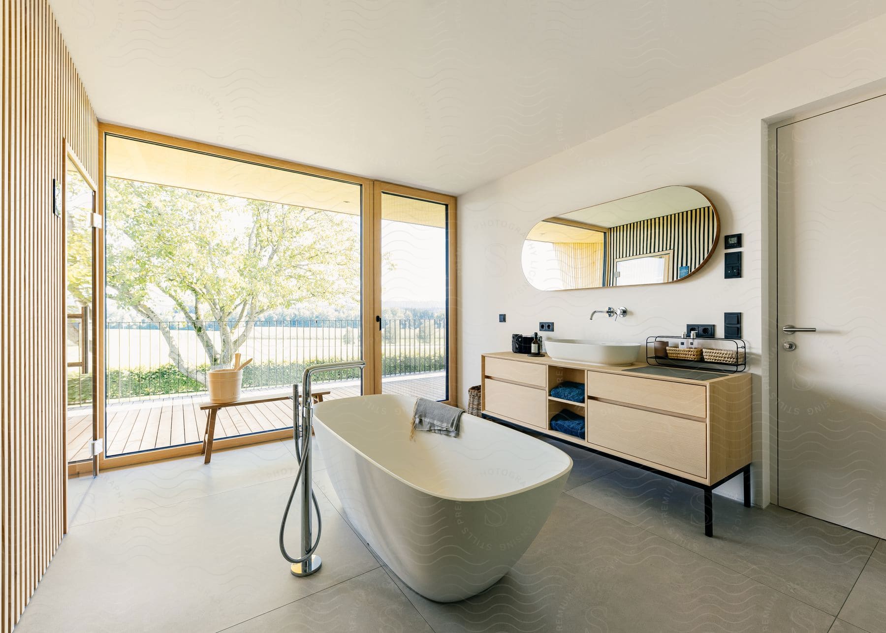 A freestanding bathtub in a modern bathroom looking out over a wooden patio.