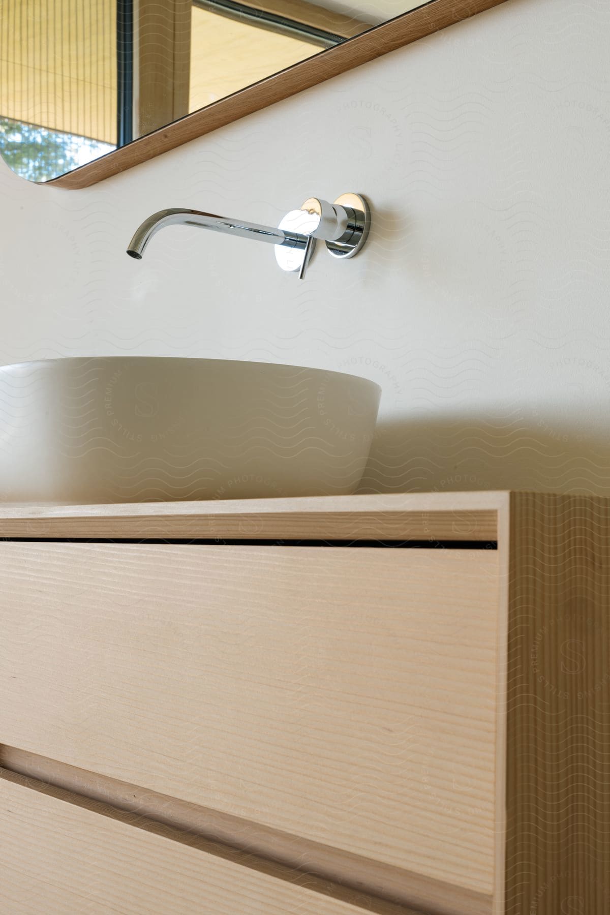 A bathroom bowl sink on top of a wood vanity with a faucet coming out of the wall