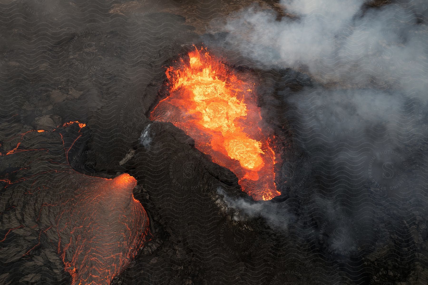 An aerial view of a volcanic eruption with molten lava flows and plumes of smoke.