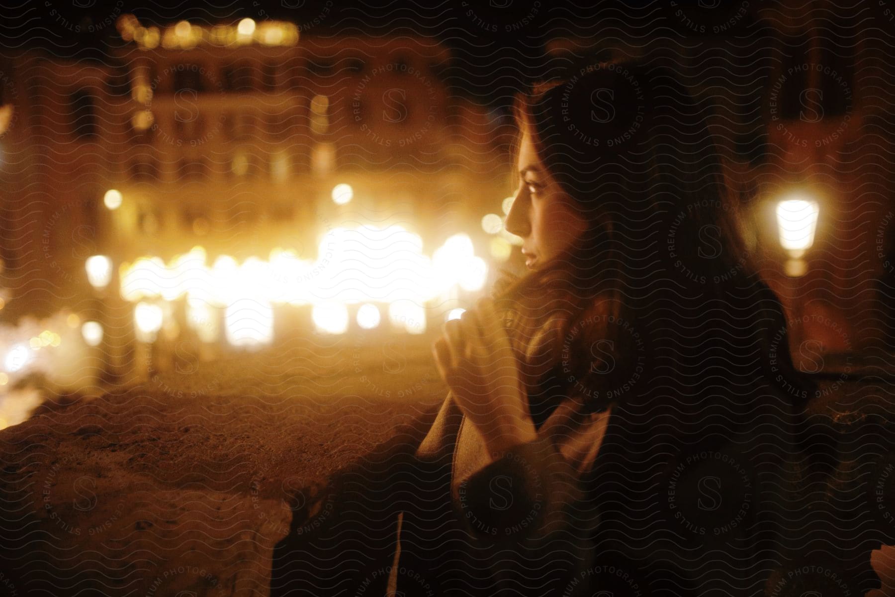 A woman playing with her hair as she walks outside and watches from afar a city street decorated with party lights