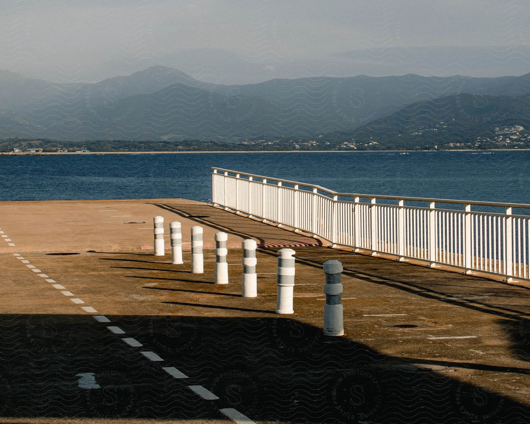 White fence along a coastal road with houses on the mountains across the river under a foggy sky