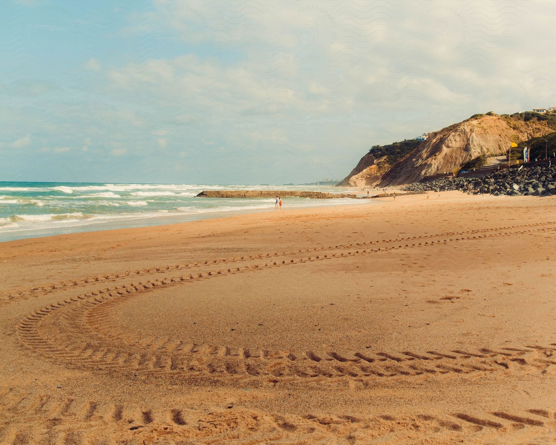 Tire tracks mark the sand near people wading into the ocean water