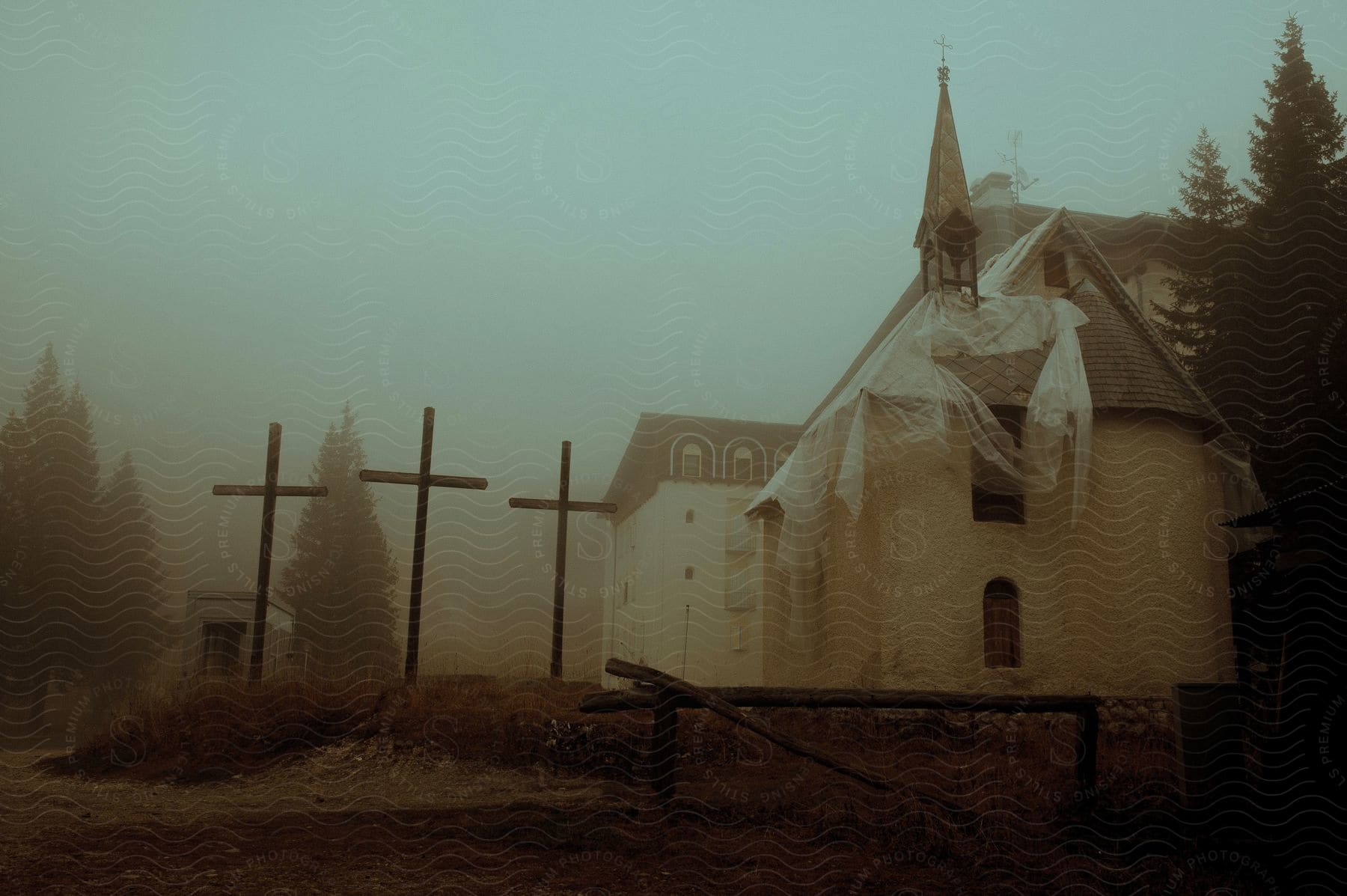 Three crosses stand outside of a rural church on a foggy evening