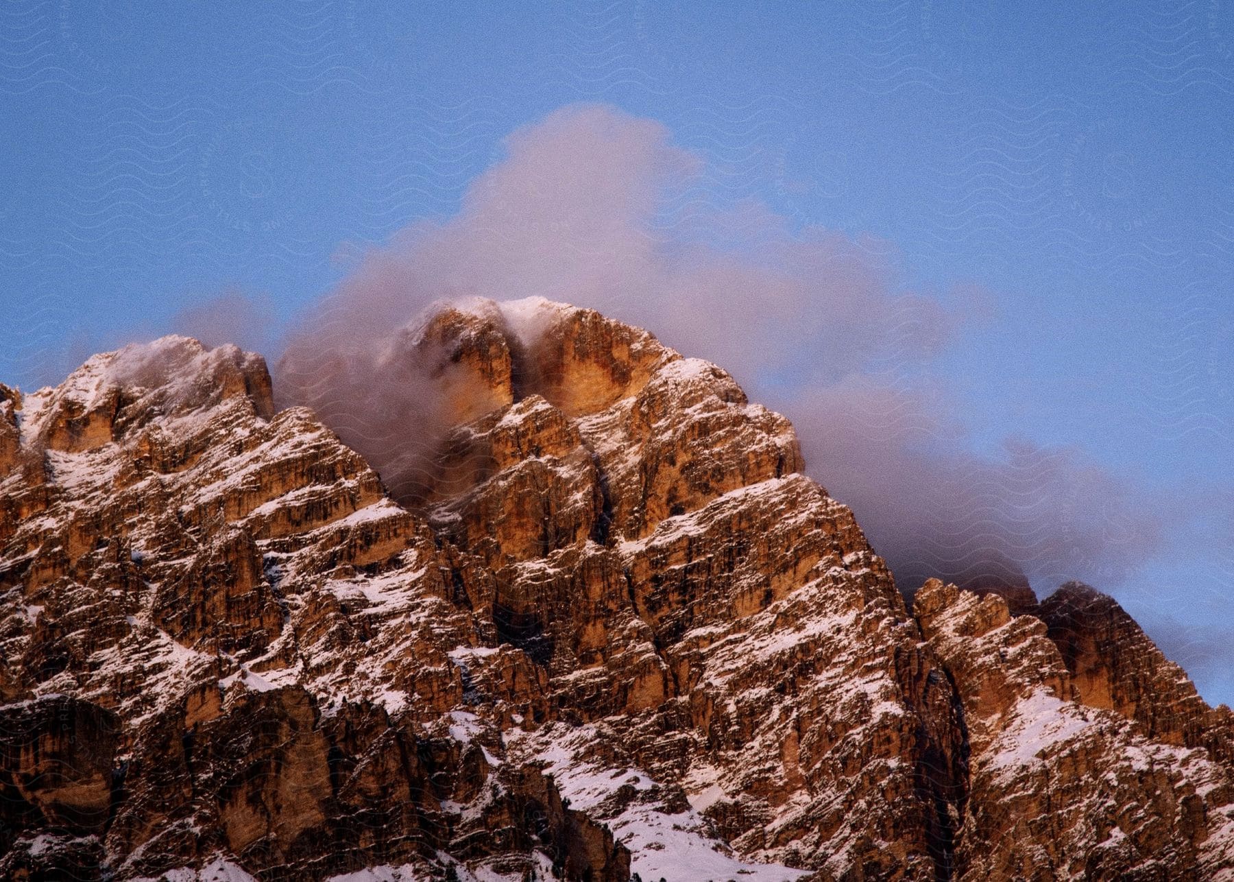 A snow-capped peak pierces a clear blue sky, its jagged silhouette dusted with a wispy cloud.