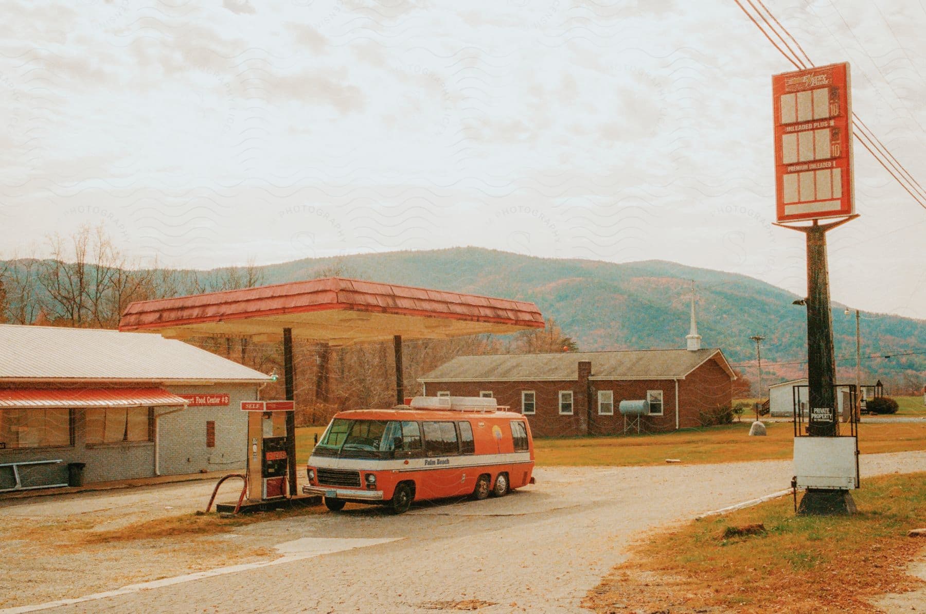 An orange motorhome is parked in an abandoned gas station in a small town on an autumn day.