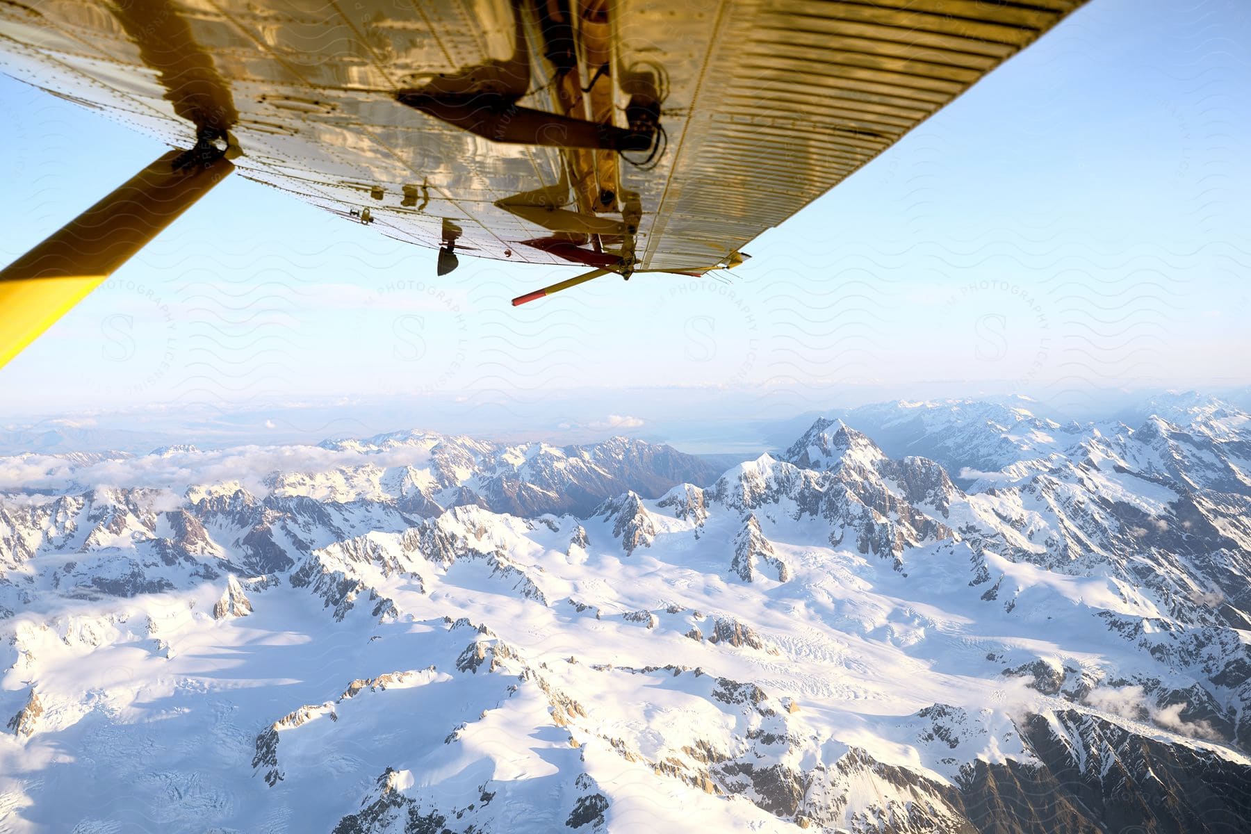 View from under an airplane wing of snow covered mountains across the landscape