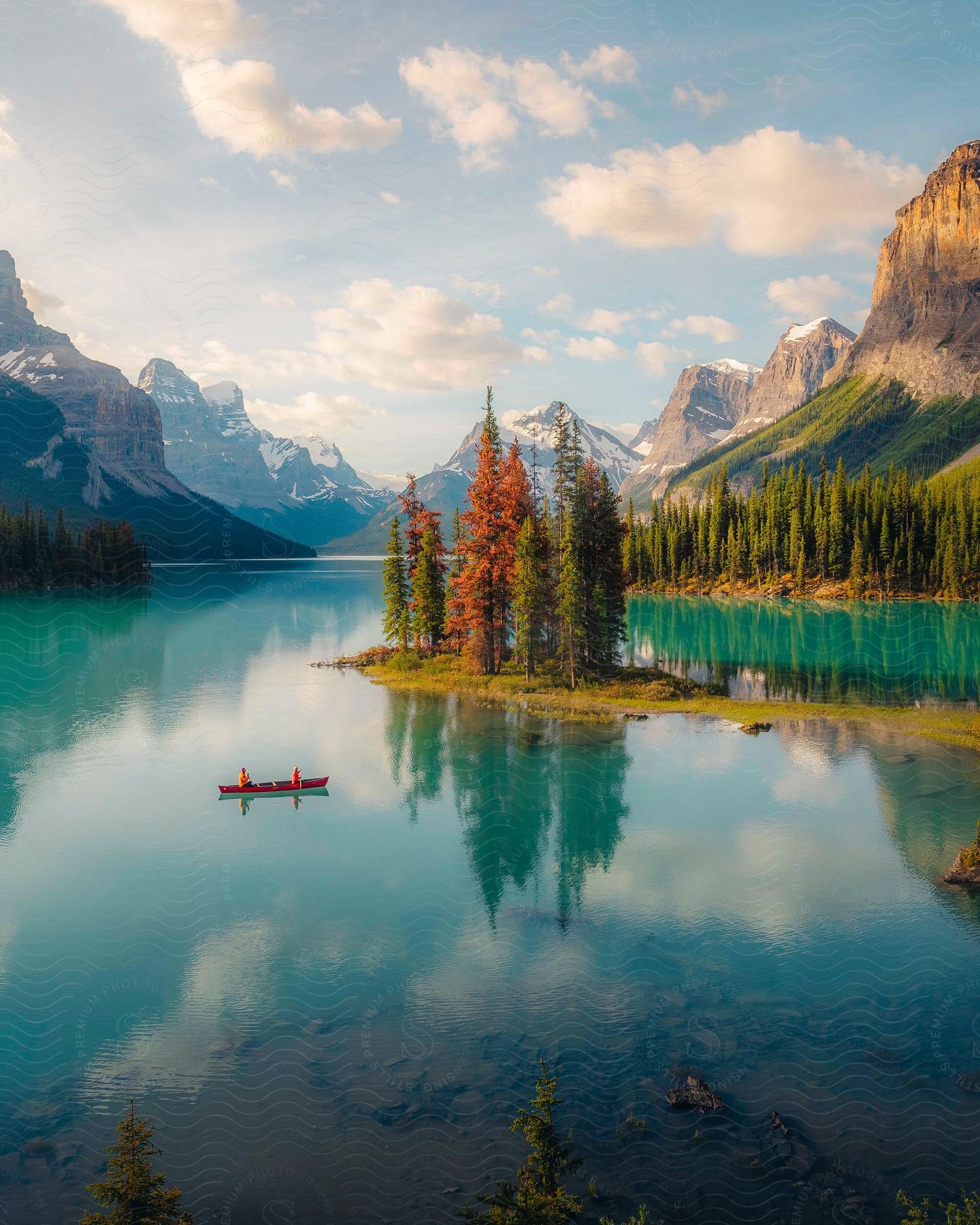 Two People Canoeing At Maligne Lake Where The Clear Water Reflects The Trees And Surrounding Mountains