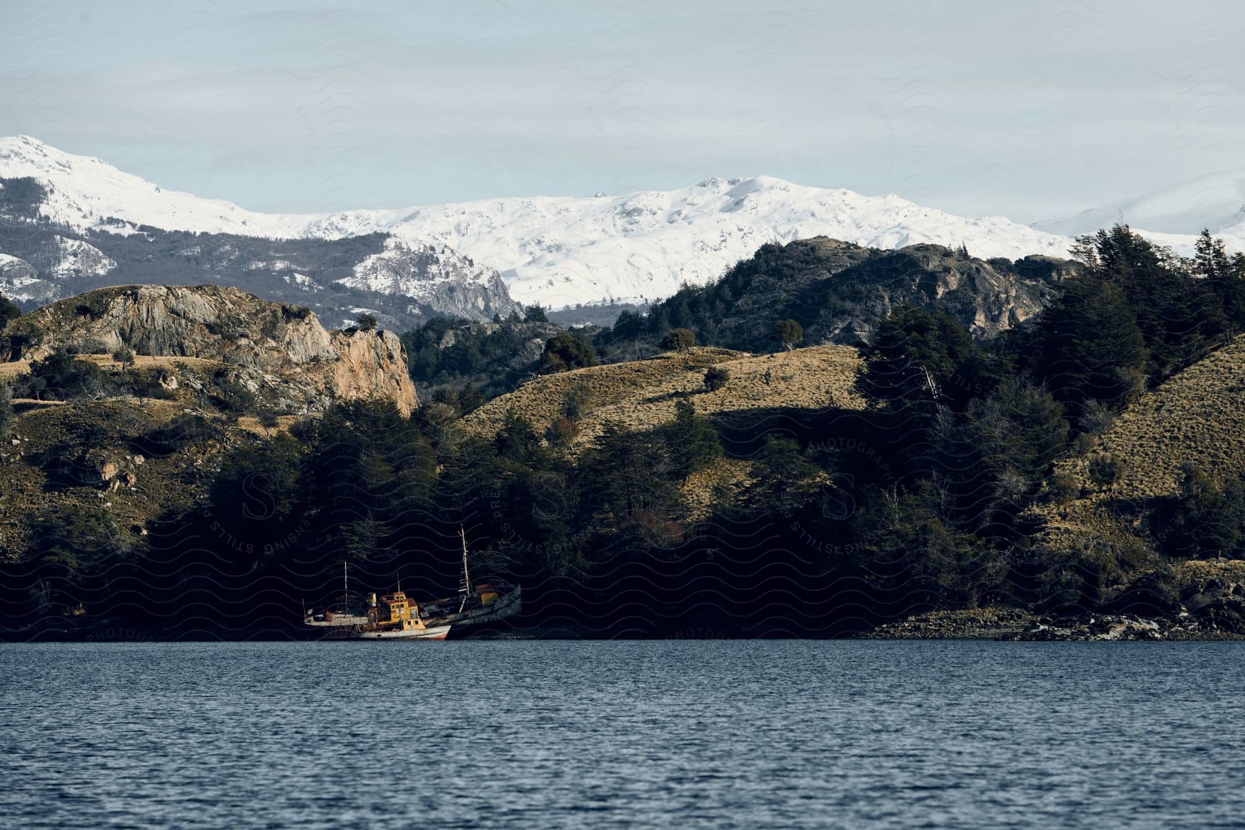 Two watercrafts float near mountainous coast on a cloudy day.