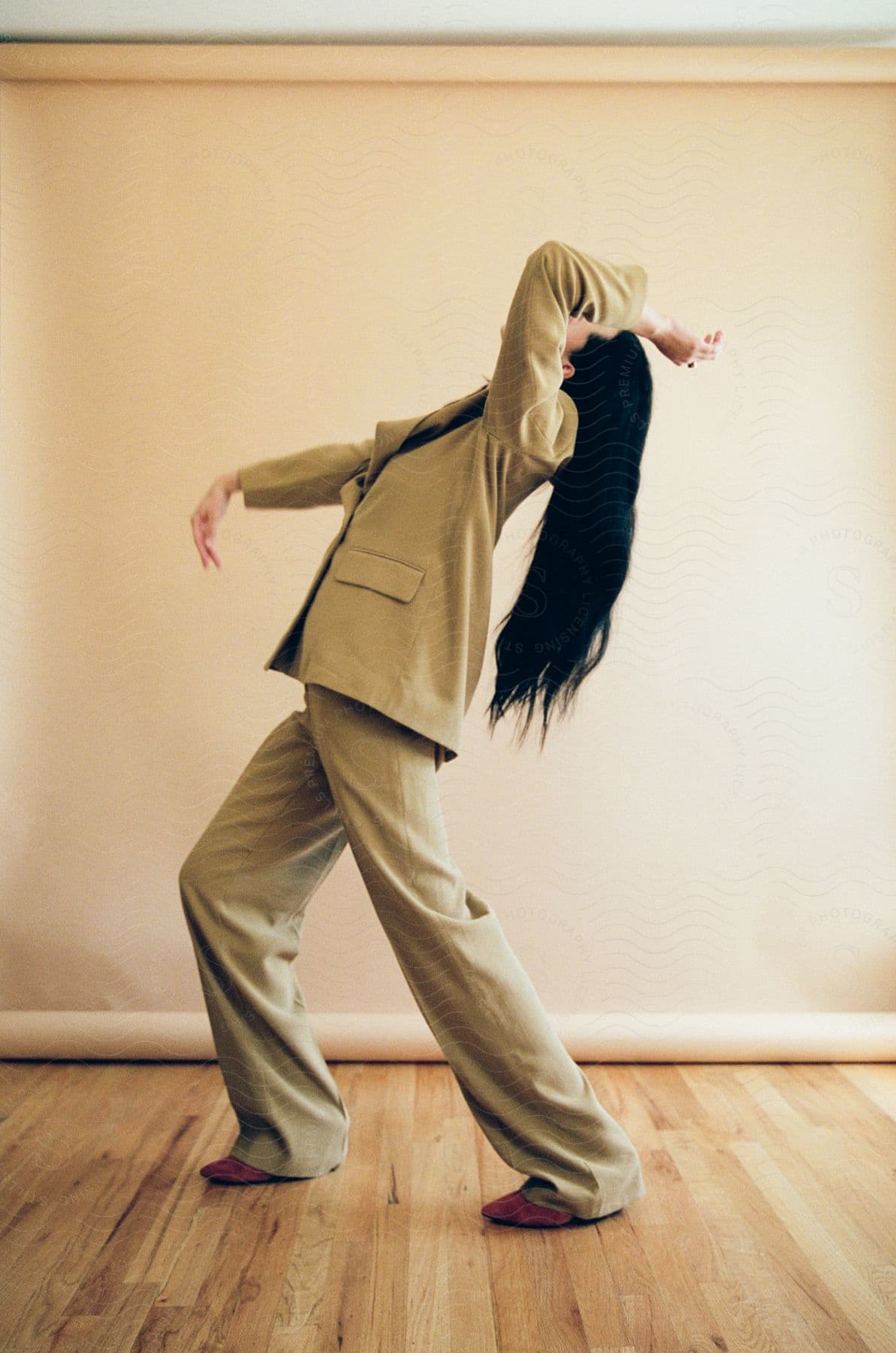 A woman is standing in a room dancing with an arm over her head bending back as her long black hand hangs down