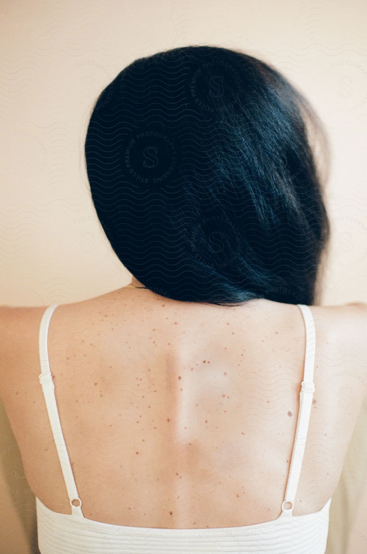 The back of a woman with black hair wearing a white top.