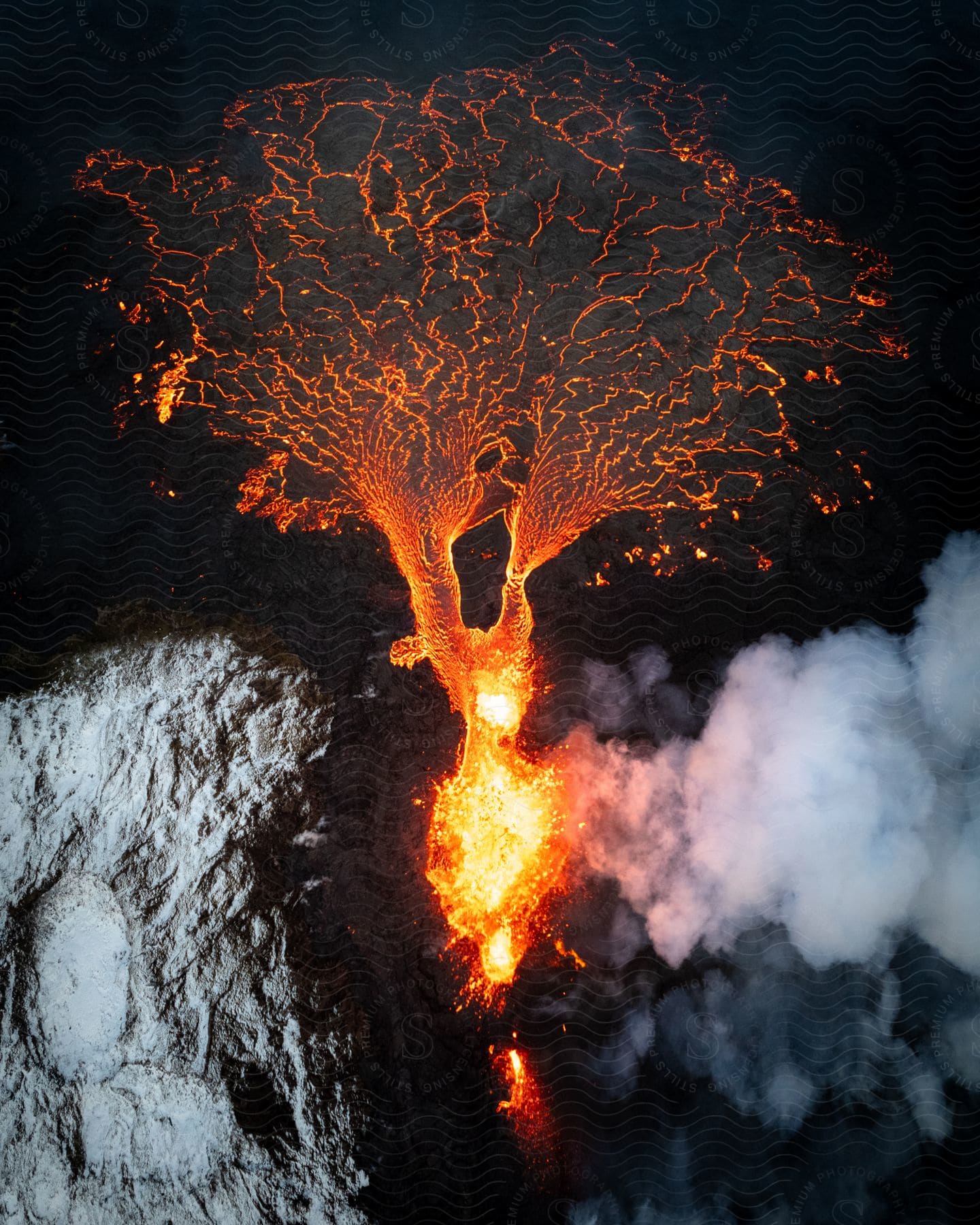 Aerial of a volcano erupting as lava spills outward at night.