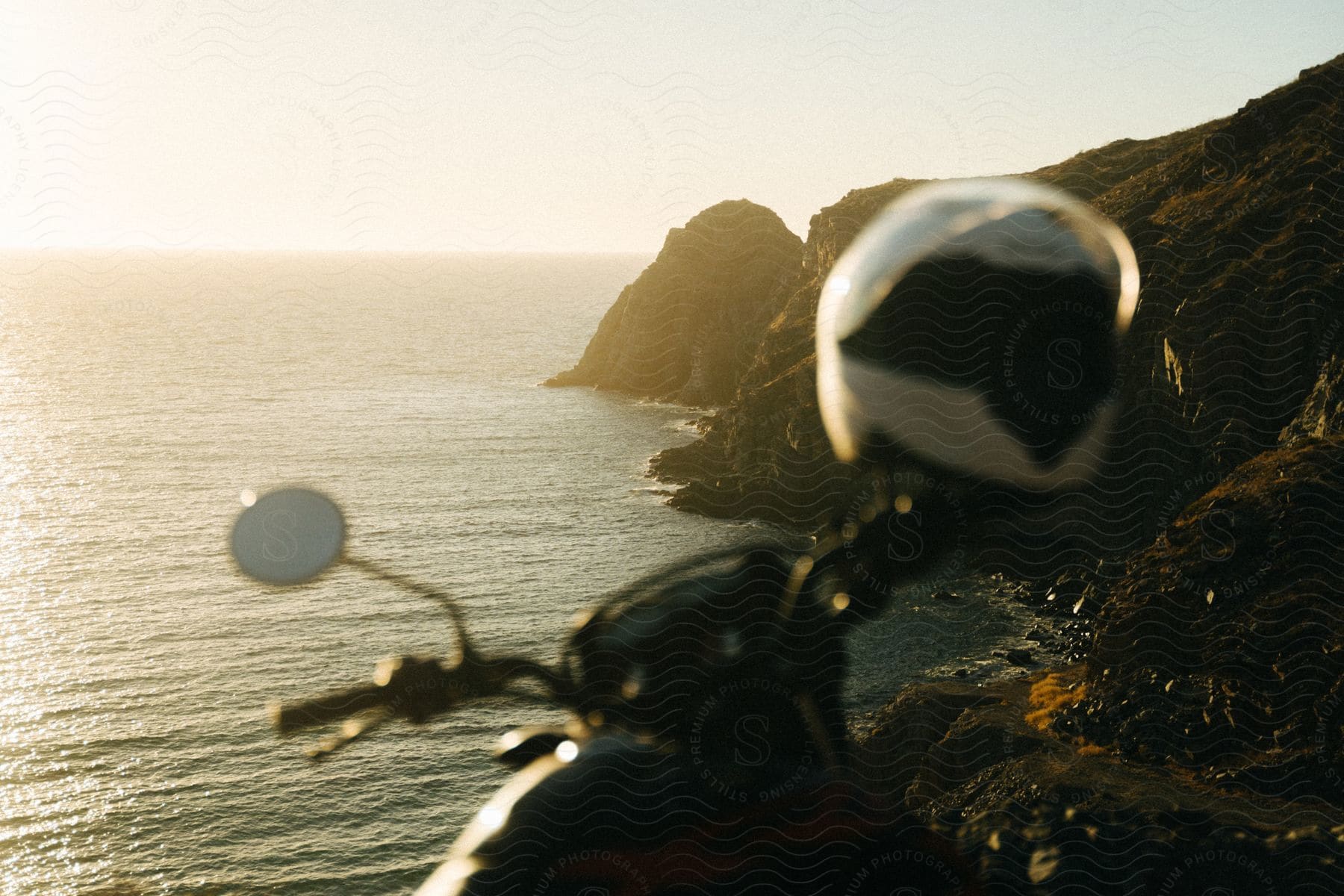 A helmet on the handlebars of a parked motorcycle overlooking oceanside cliffs and coast