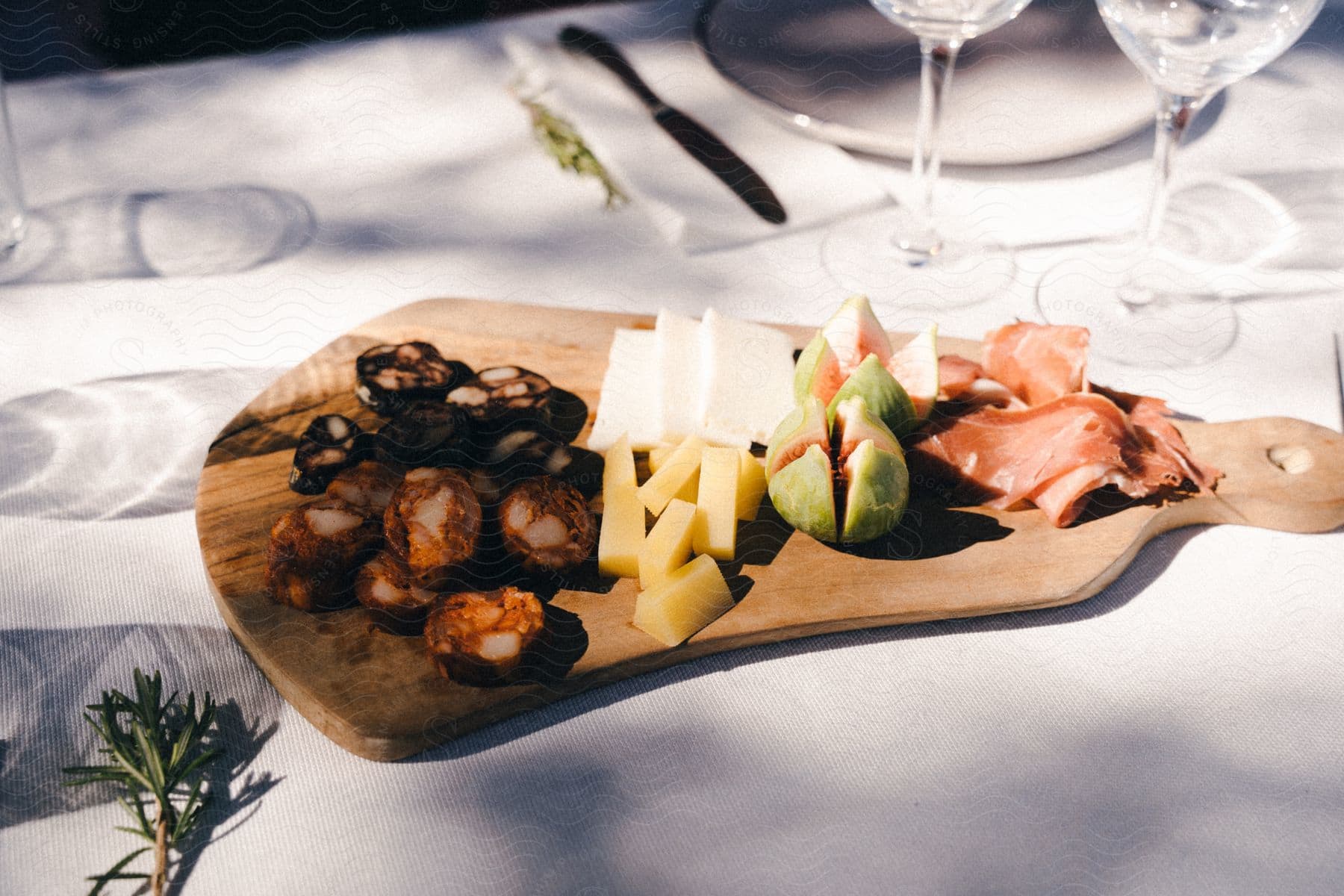 A charcuterie board contains slices of fruits and meats on a white dining table.