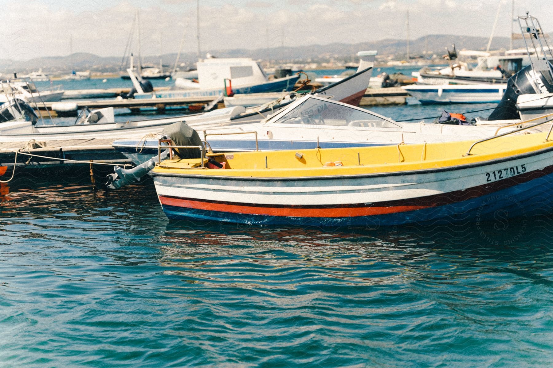 A boat with yellow and red colors is parked in a marina in the water with several other boats