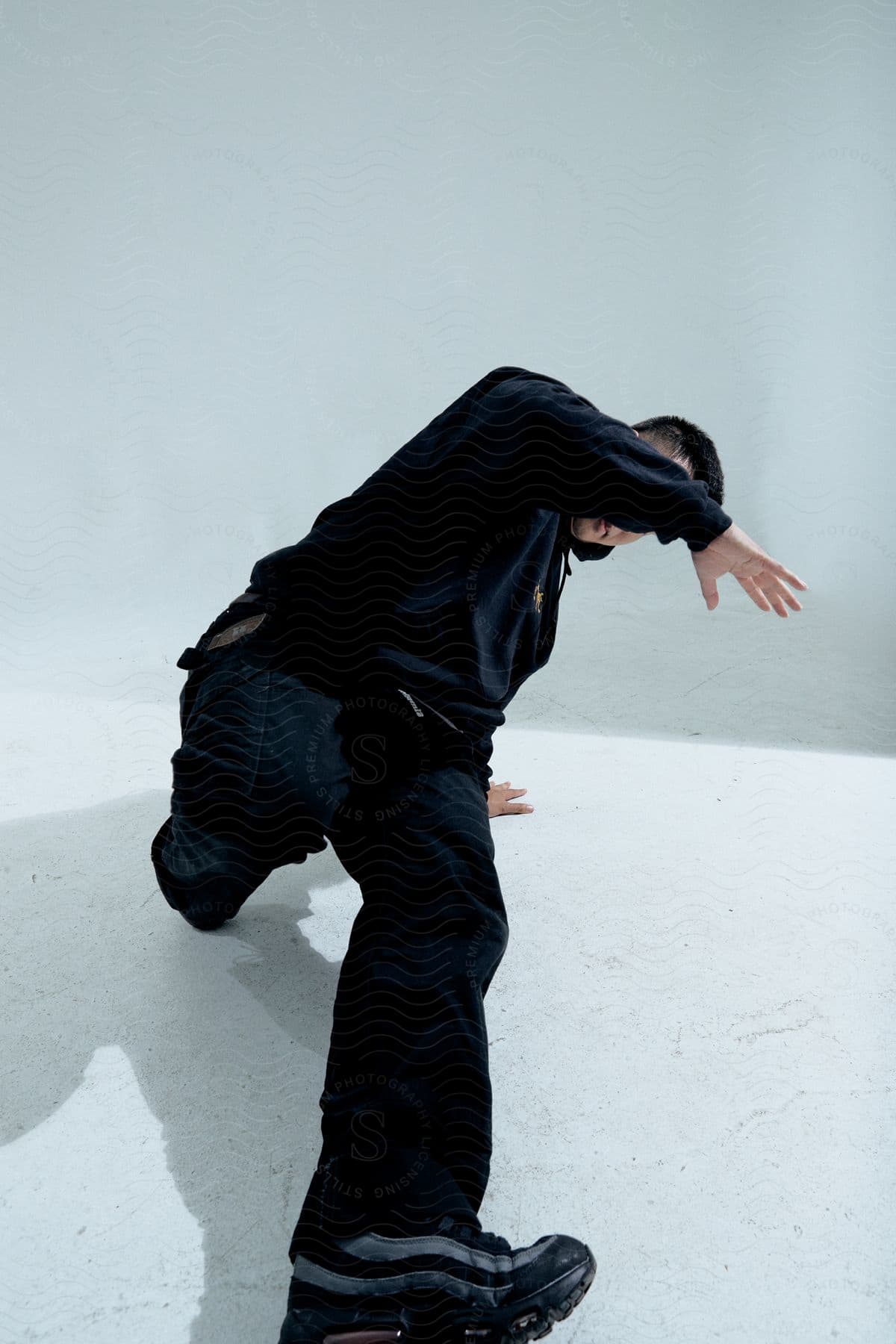 Stock photo of a person is captured mid-movement in a dance pose, wearing a black outfit against a grey background.