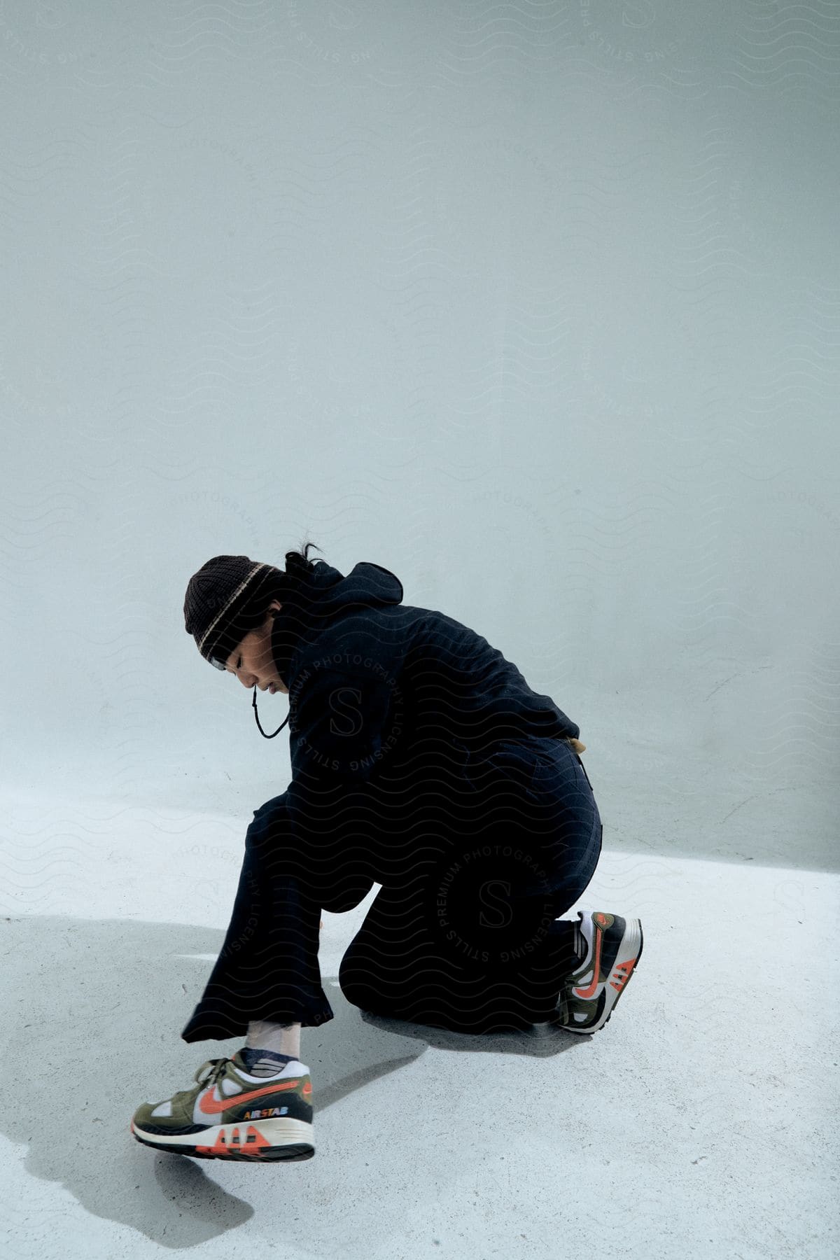 Stock photo of a dancer wearing a black hat, hoodie, and pants dances on a white platform.