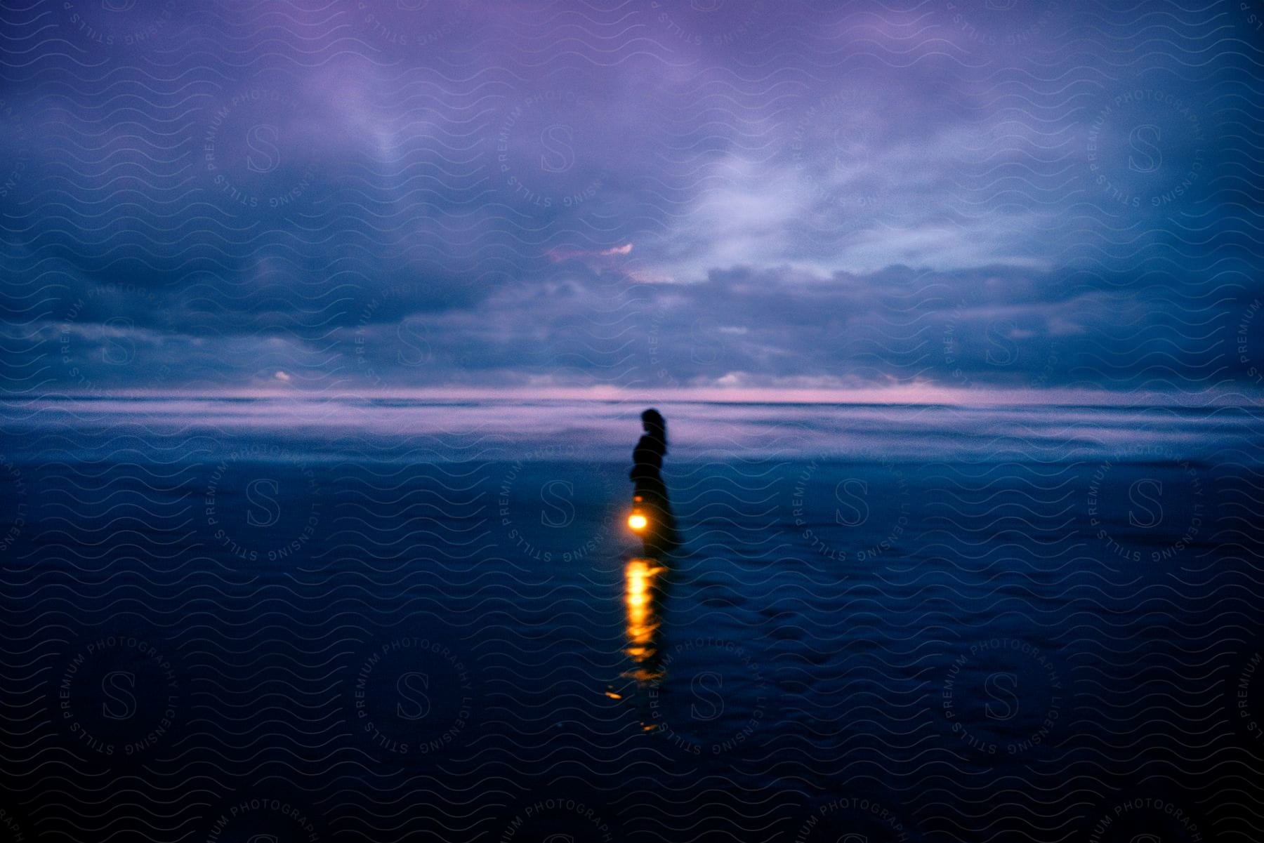 A person on the beach holding a lamp during dusk.