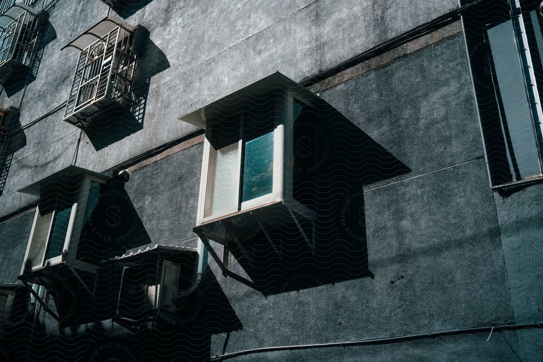 Sunlight shines on the side of a tall, gray apartment building.