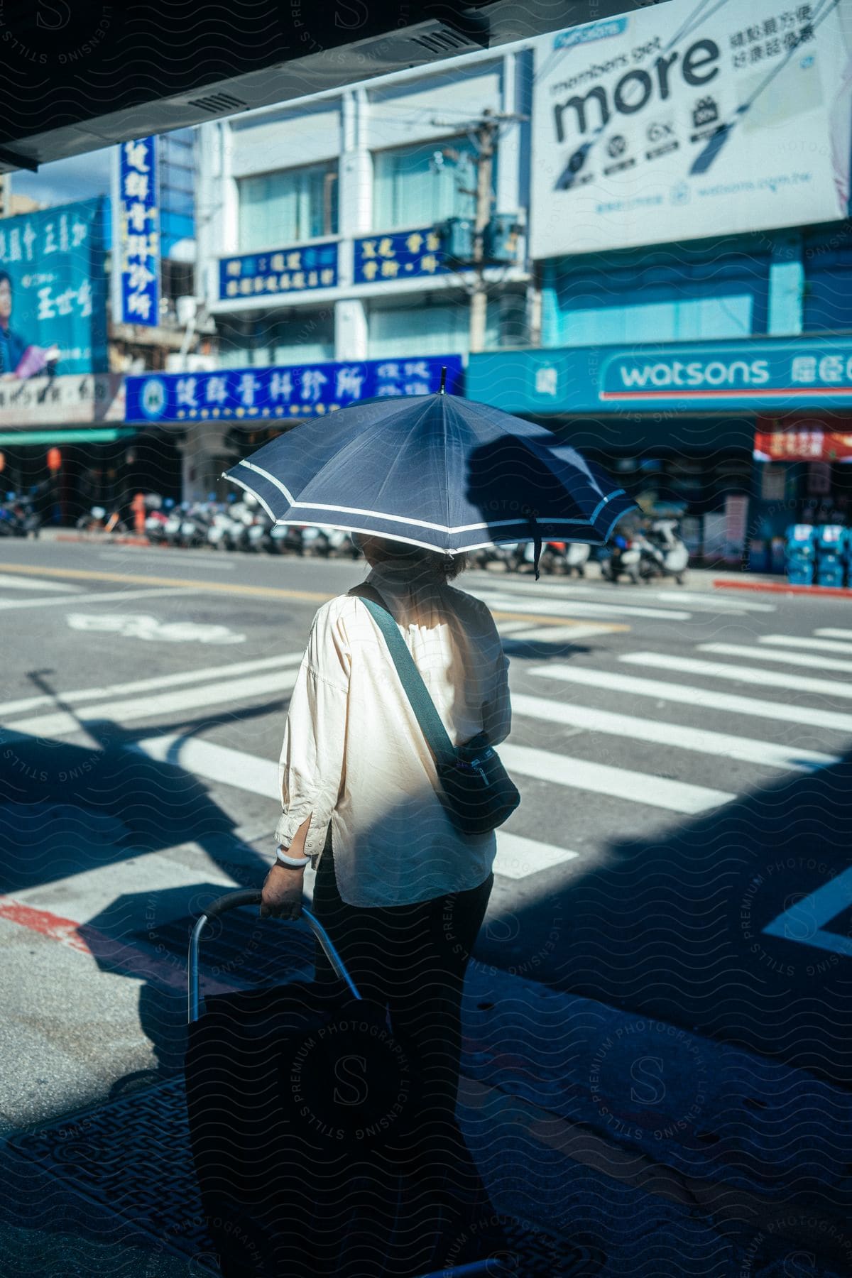 A woman walking around in a city with an umbrella on a sunny day.