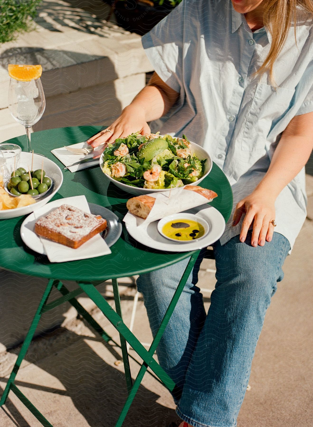 A woman having a salad, a sandwich and olives for brunch on a sunny terrace.