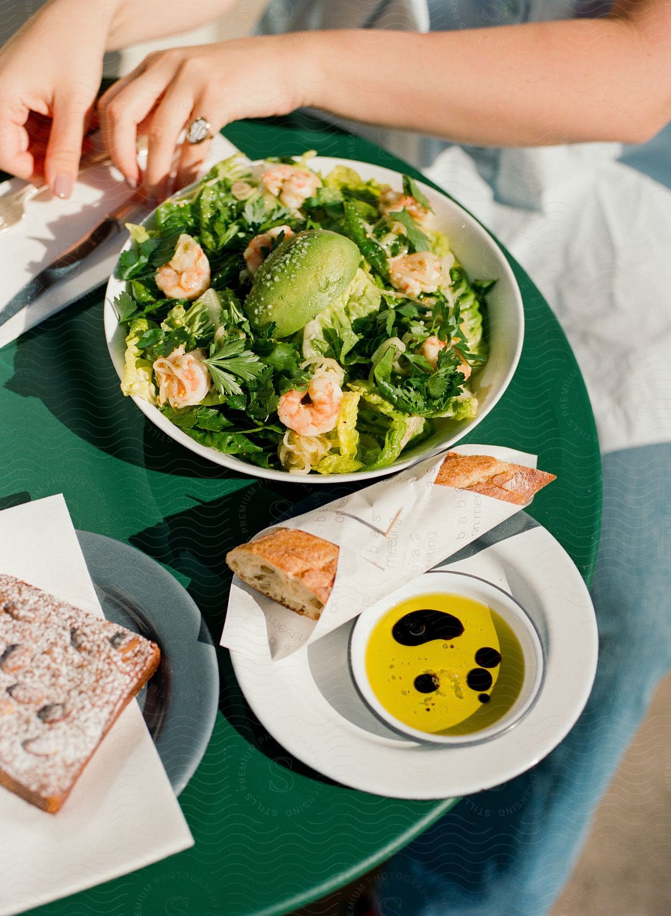 A female sits at a small dining table with fresh bread and a shrimp salad.