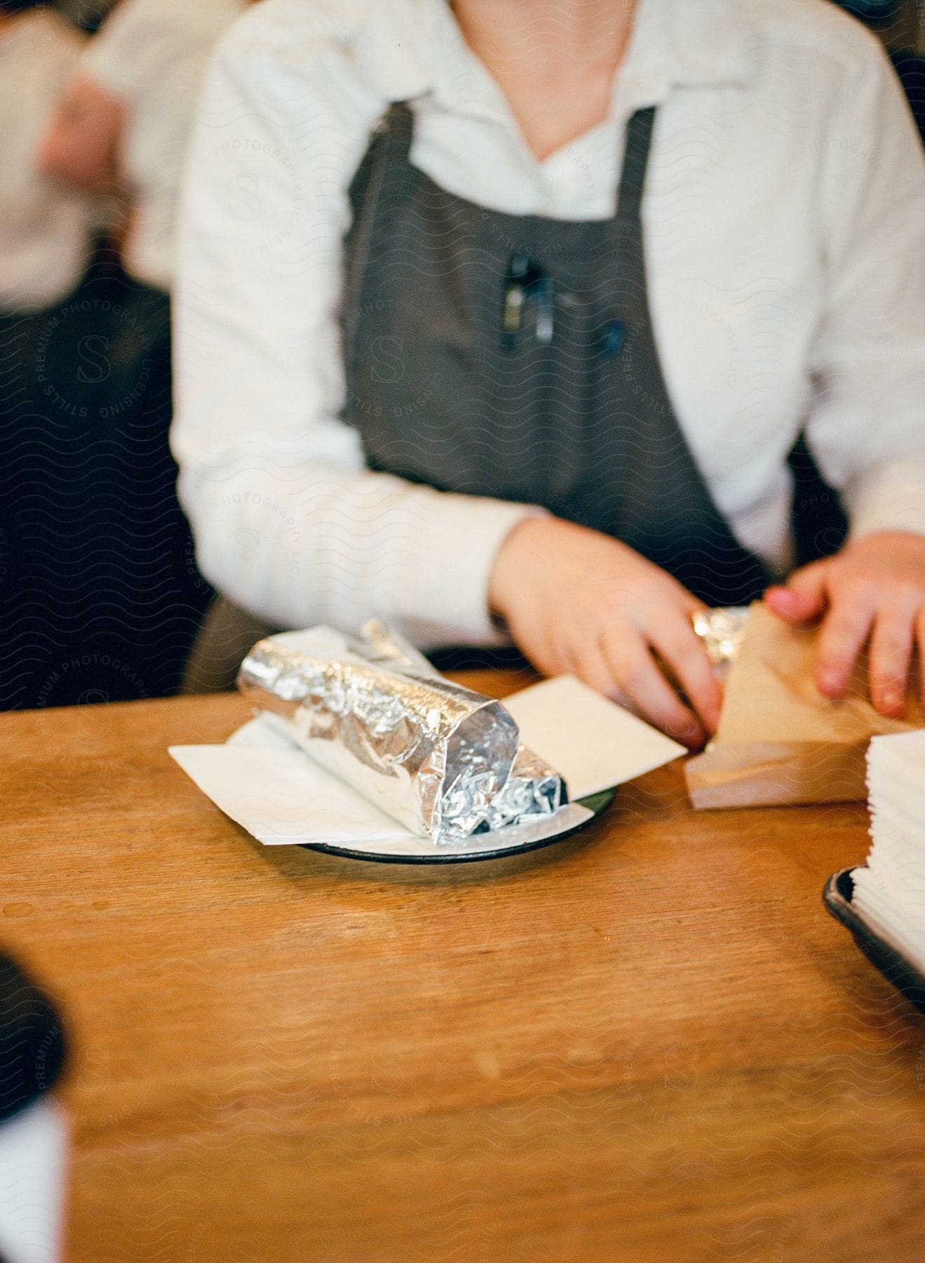 A waitress is standing at a table with food wrapped in foil on a plate