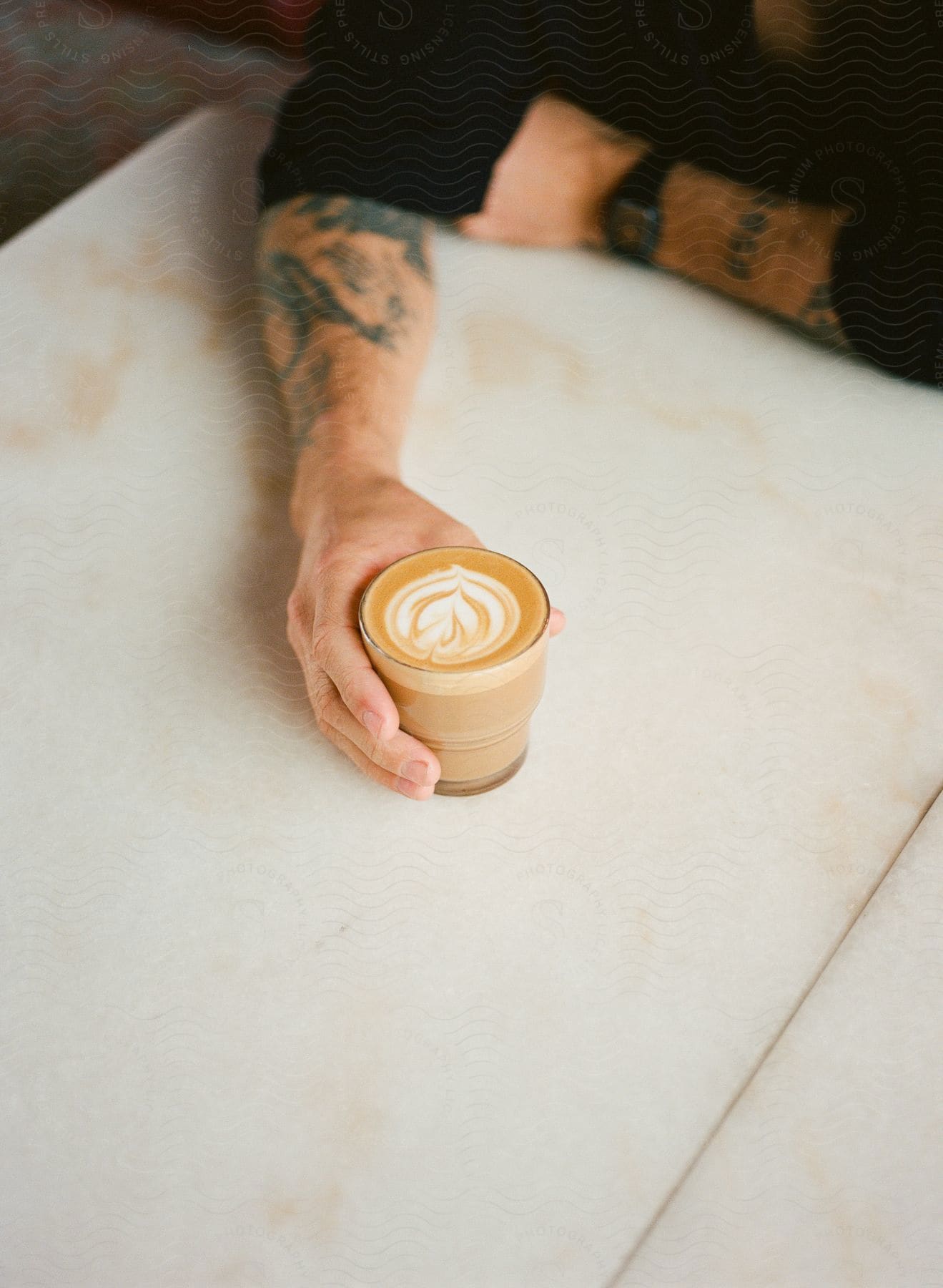 A man holds a cup of coffee while sitting at a table.