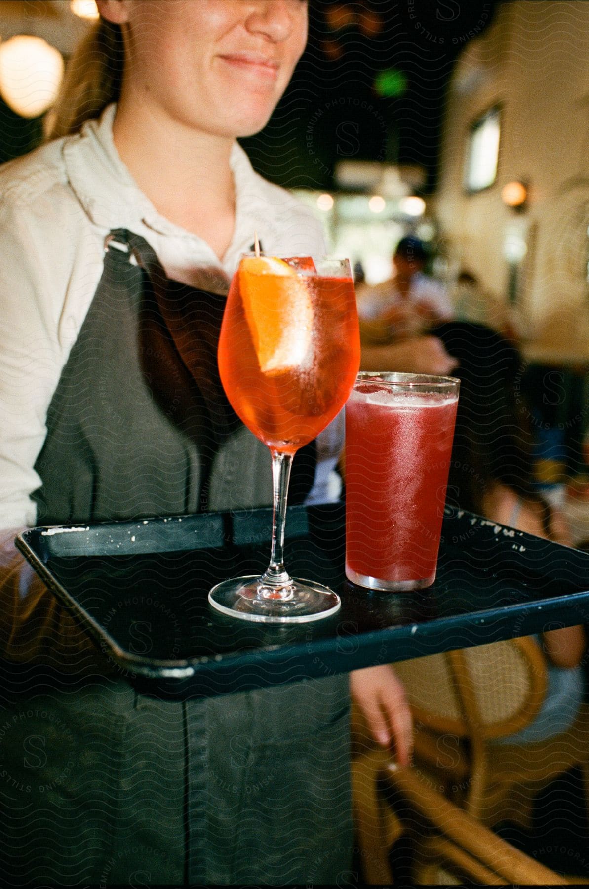 a waiter is carrying two glass of non alcoholic beverages on a tray