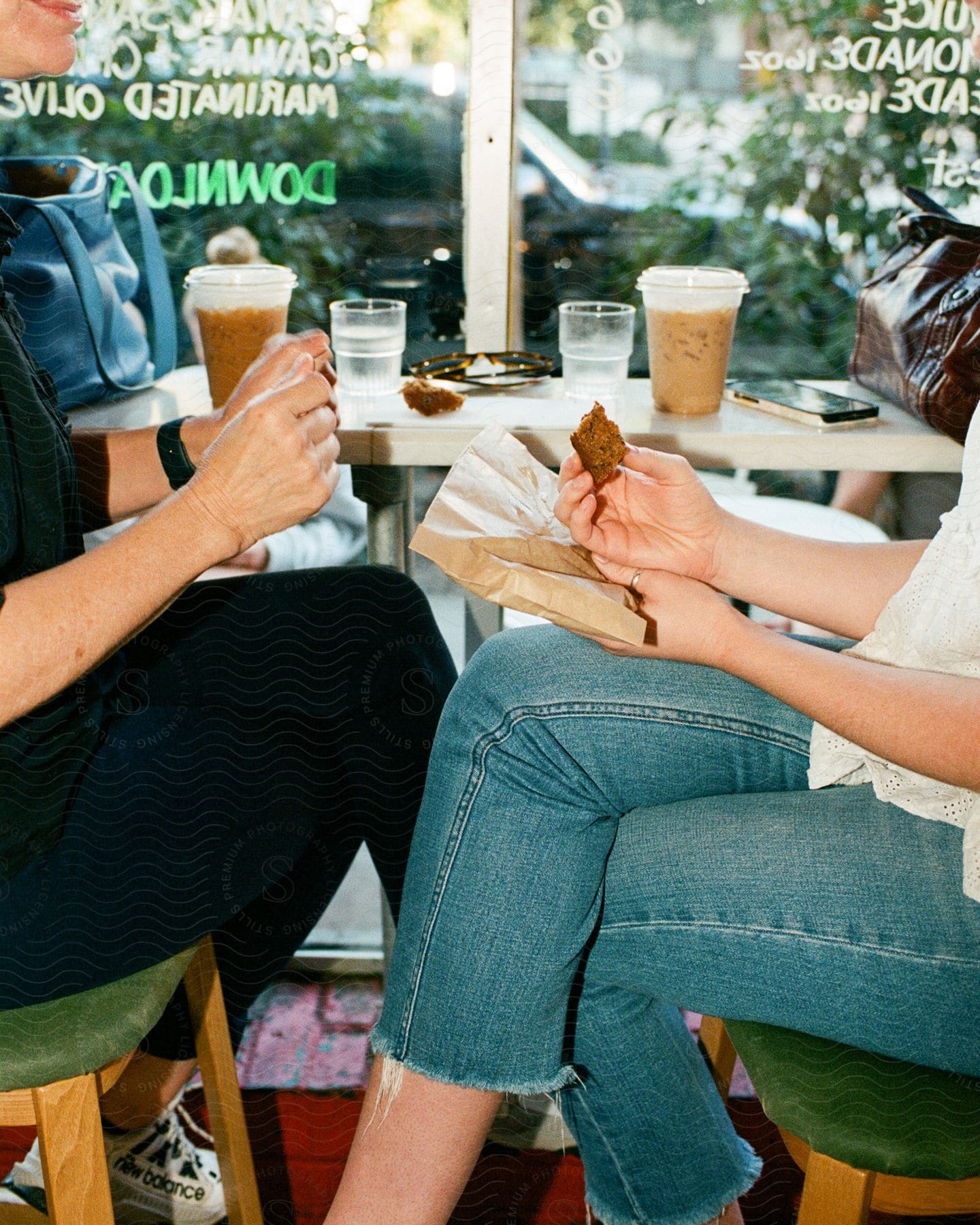 Two women sit at restaurant table with iced coffee beverages and pastries.