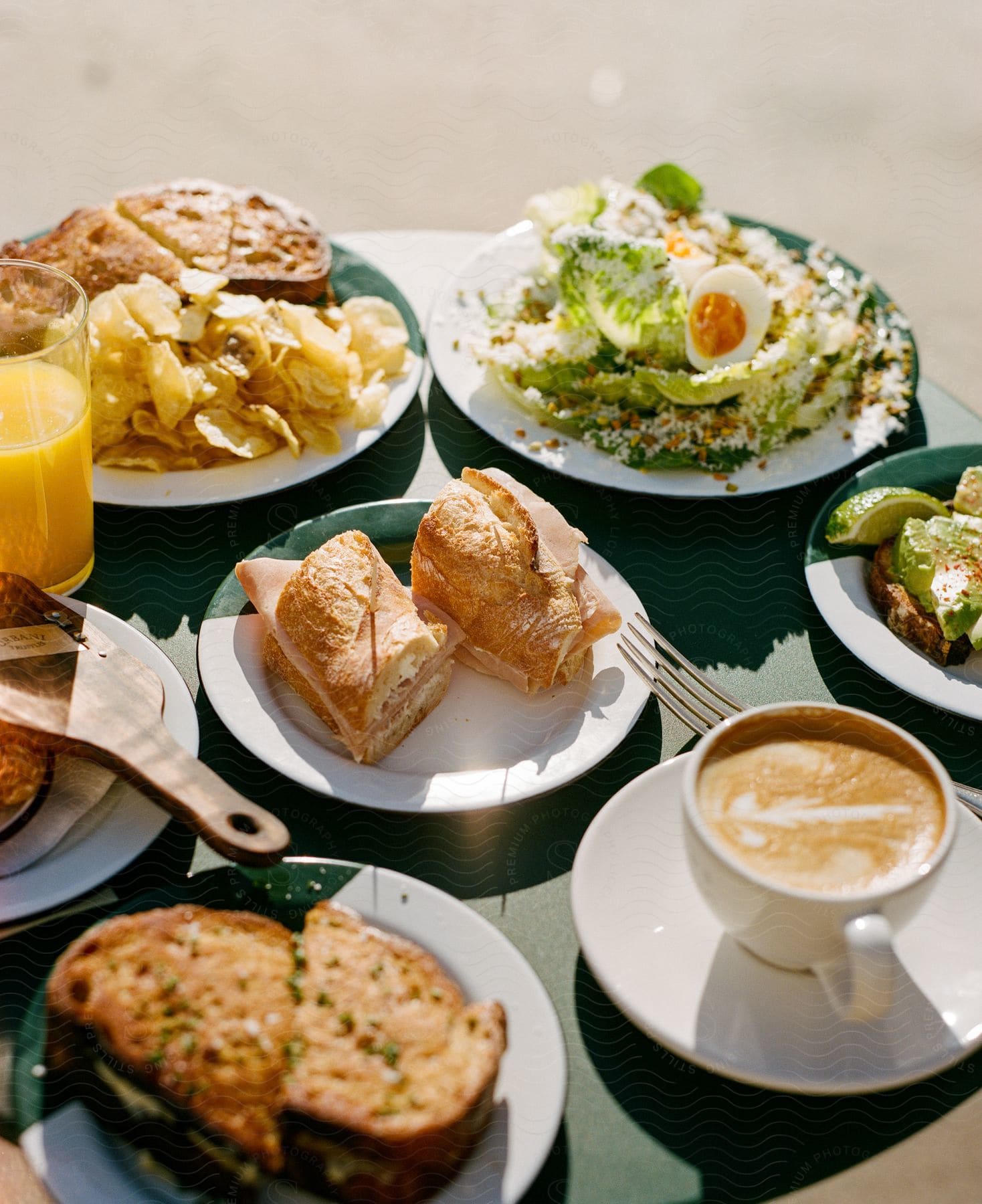 Salads, sandwiches, chips and drinks on a green table outside on a sunny day.