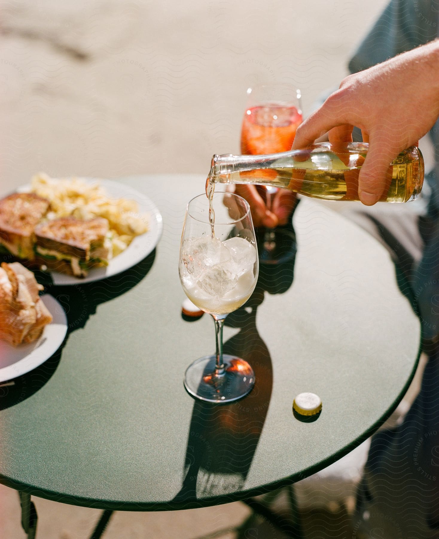 An adult pours an alcoholic beverage into a wine glass on a small table outside.