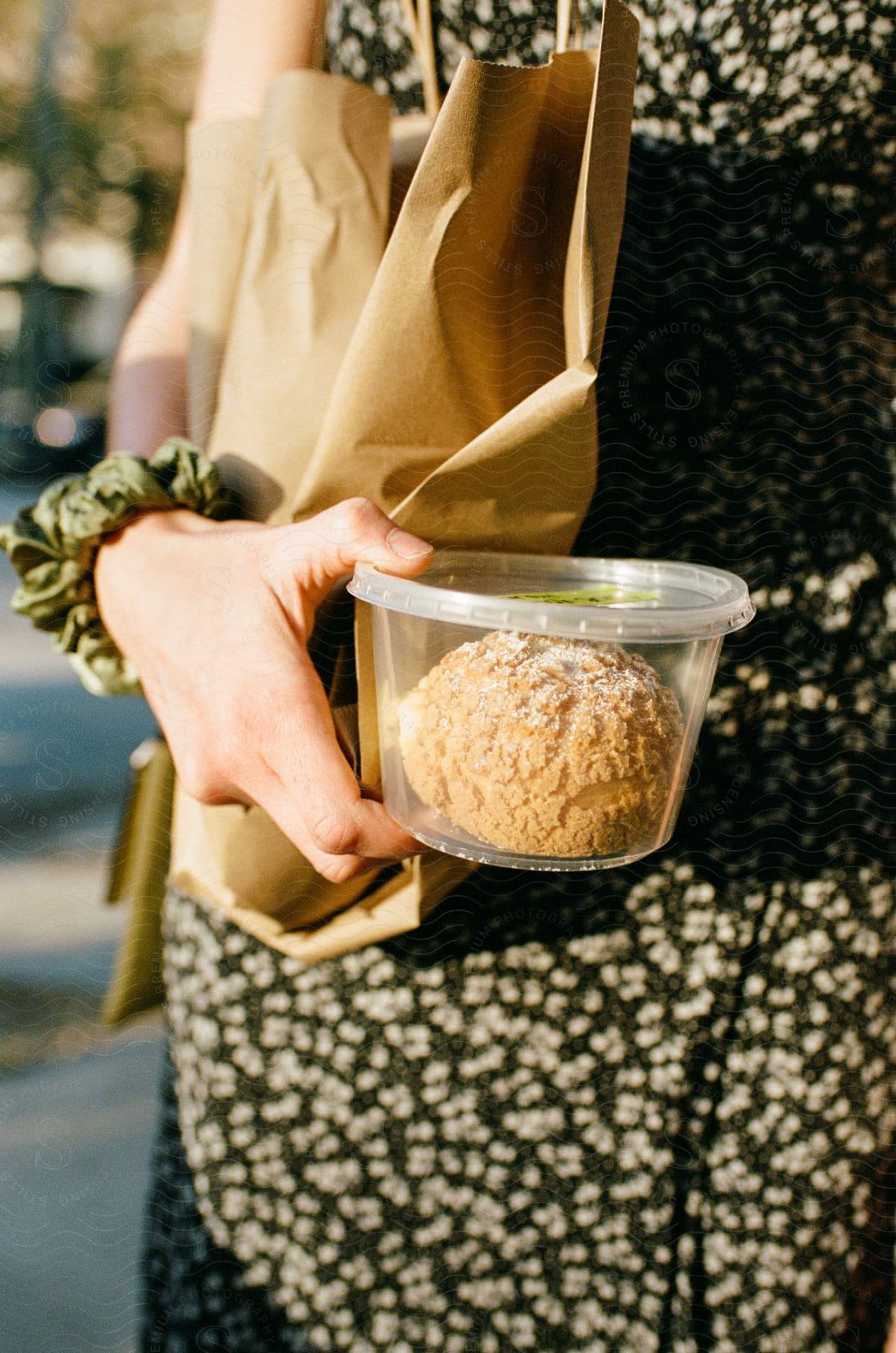A woman holds a plastic container with a biscuit inside with a paper bag under her arm