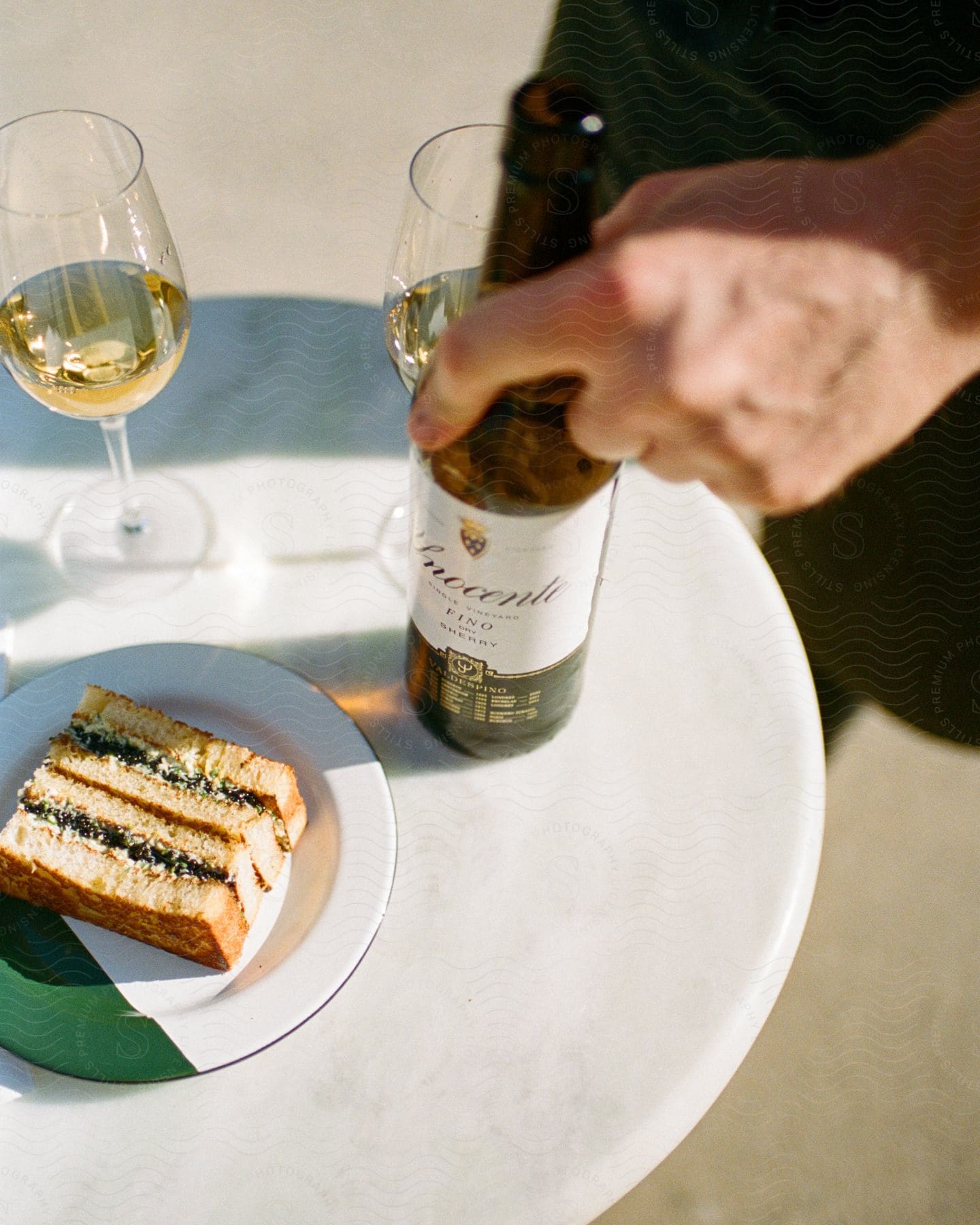 a person holding wine bottle on a coffee table with two wine glass an a plate of cake